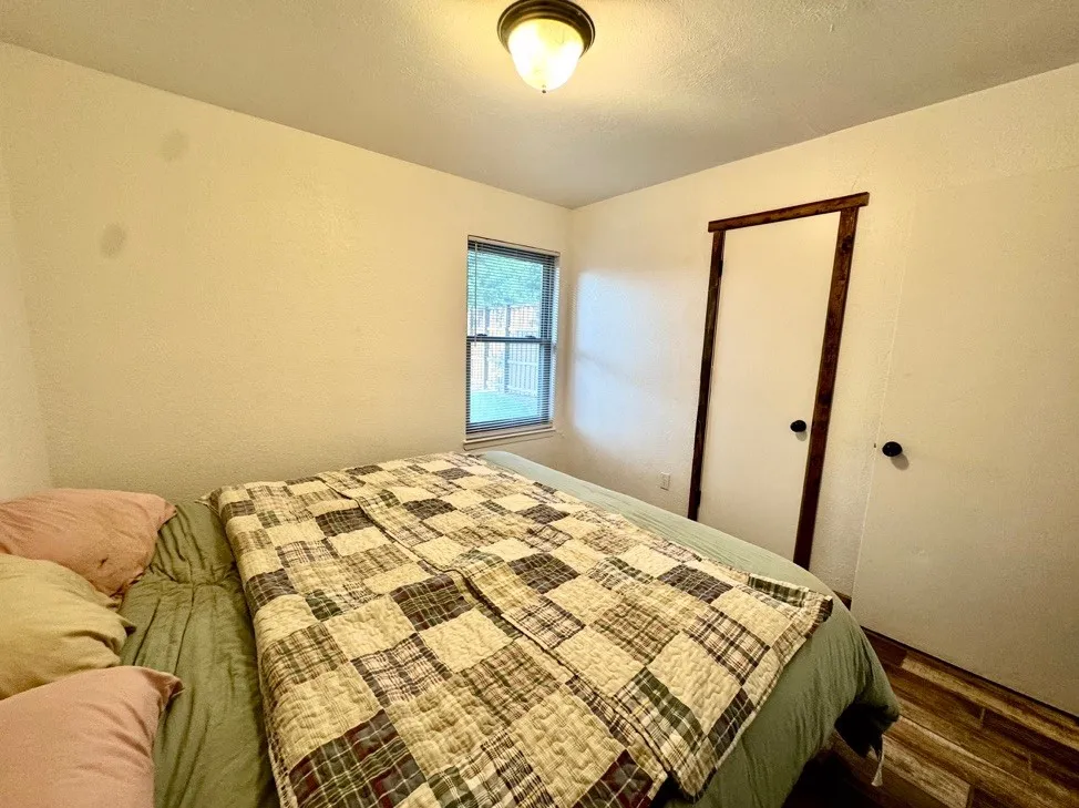 Bedroom featuring a window with exterior visibility, wood-finish flooring, and a ceiling-mounted light fixture