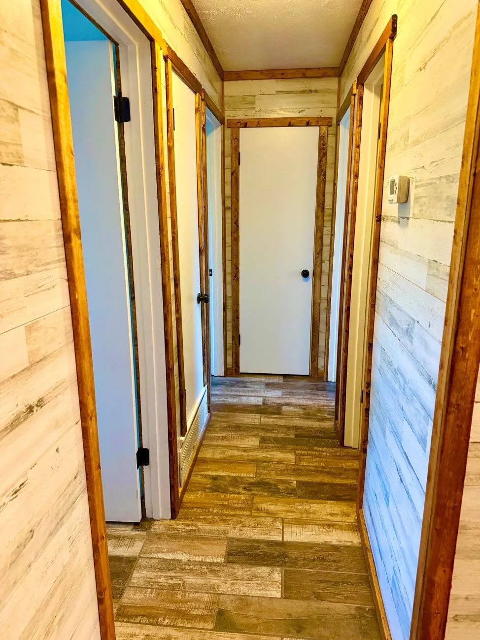 Hallway featuring wood-finish flooring, light-toned plank wall coverings, and dark wood trim