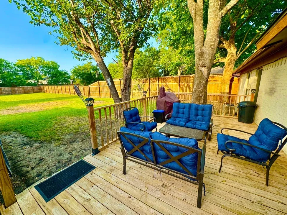 Expansive backyard featuring a wood deck, wood privacy fencing, a manicured lawn, and mature trees