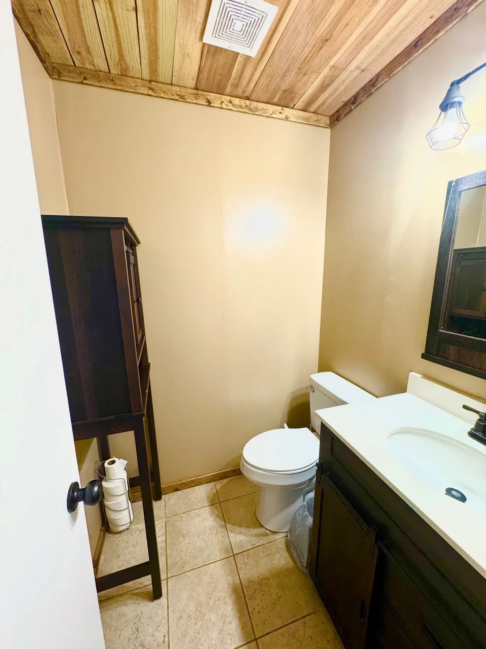 Powder room featuring a wood-finish plank ceiling, tile flooring, and a dark wood-finish vanity with a white countertop and integrated sink