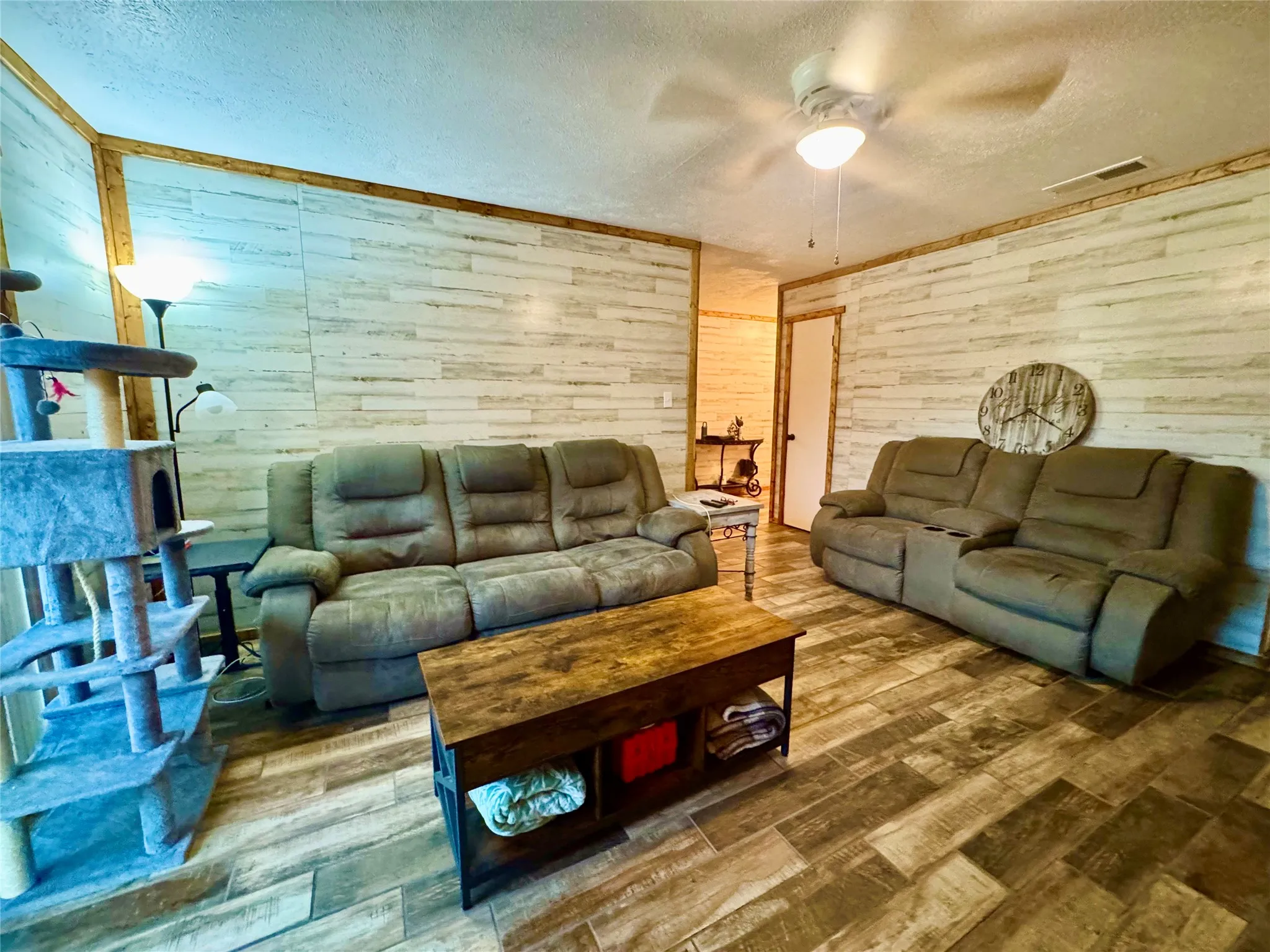 Living area featuring wood-finish flooring, accent wall paneling, wood trim, and a ceiling fan with integrated lighting