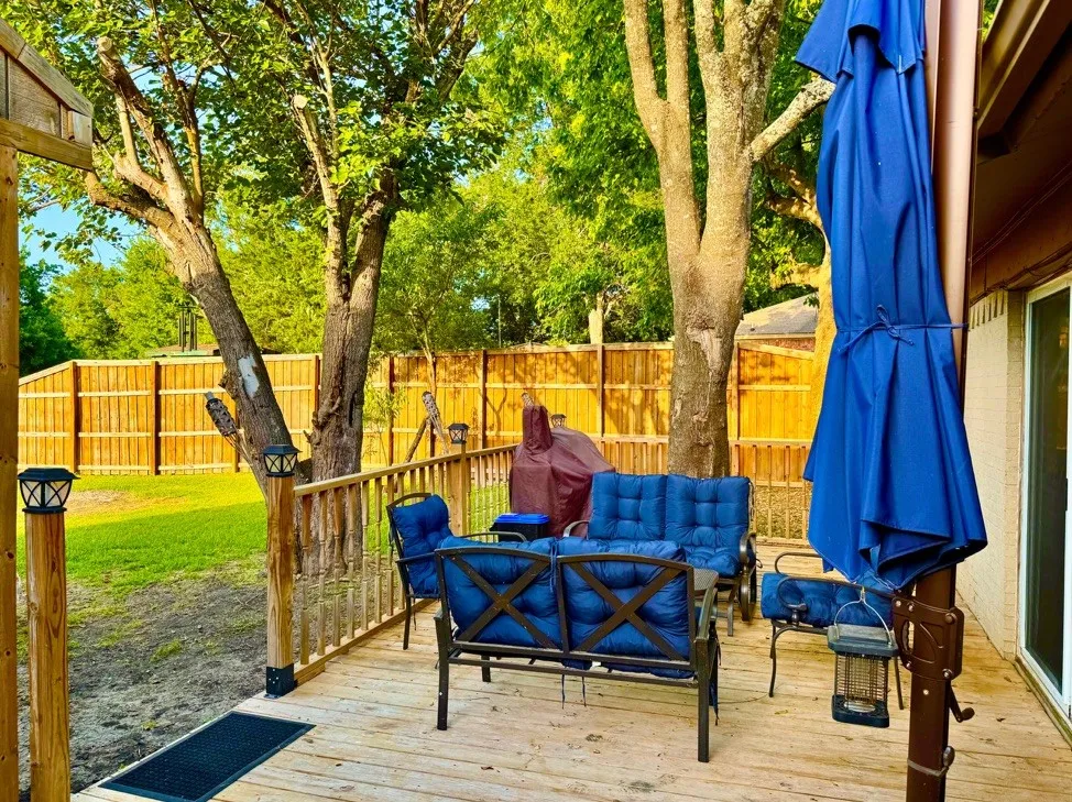 Wood deck with railing, featuring a privacy fence, mature trees, and a grassy area