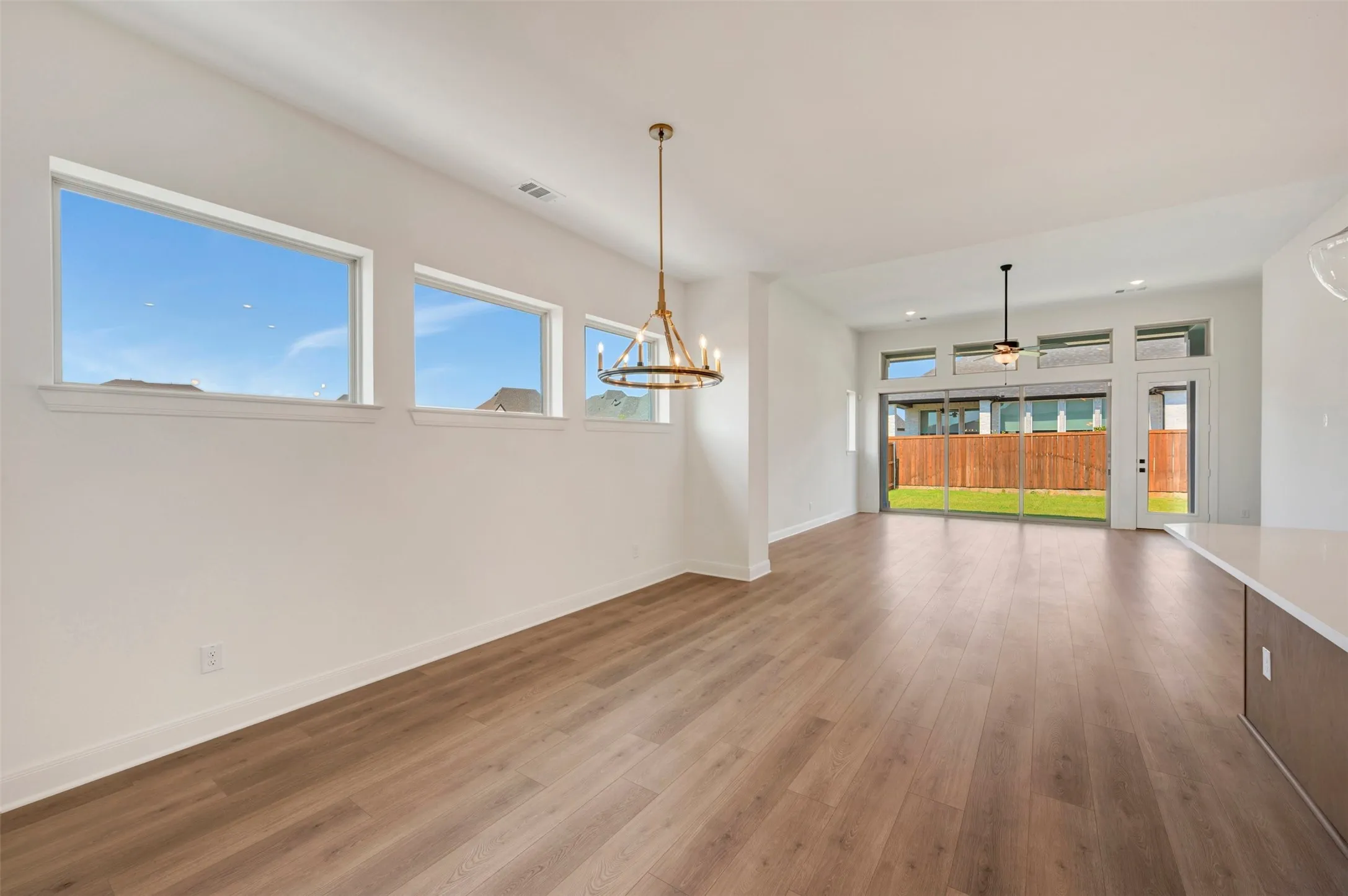 Wood-finish flooring throughout, white walls, multiple windows providing ambient light, modern chandelier fixture, and sliding glass doors to the exterior