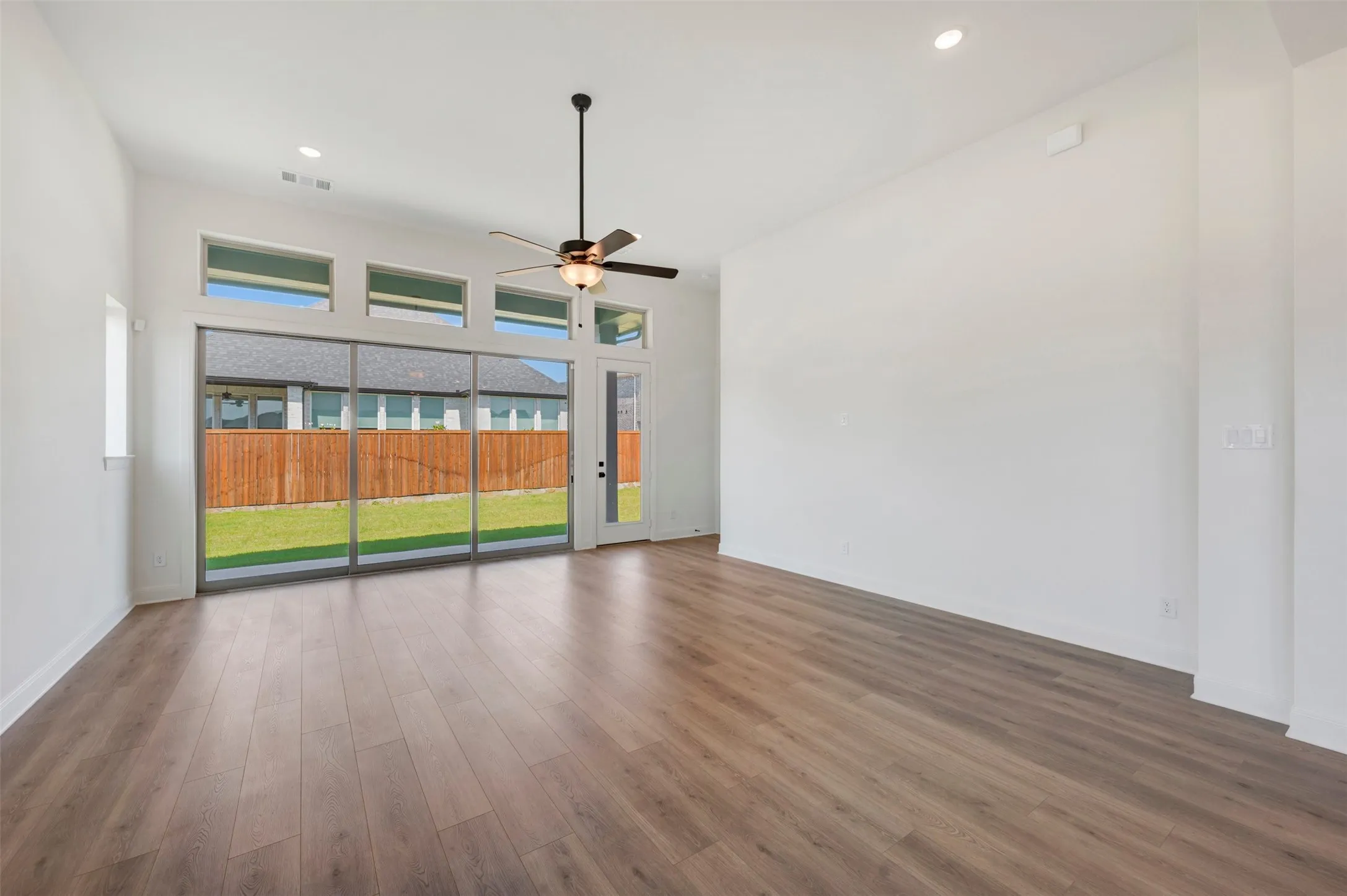 Spacious room featuring wood-finish flooring, a ceiling fan, and recessed lighting