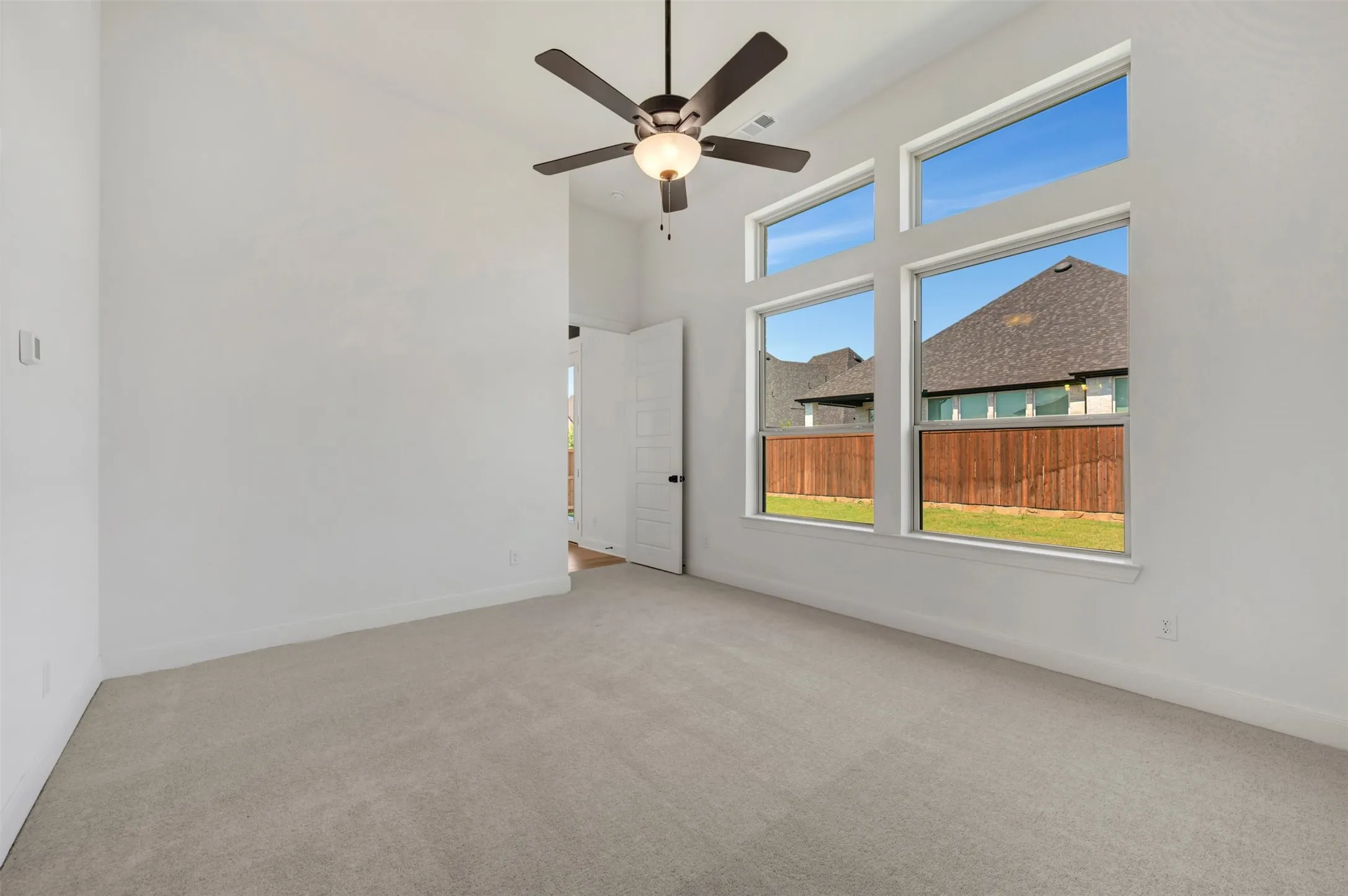 Carpeted flooring, vaulted ceiling, multi-panel windows, ceiling fan with integrated lighting, and an interior door with dark hardware