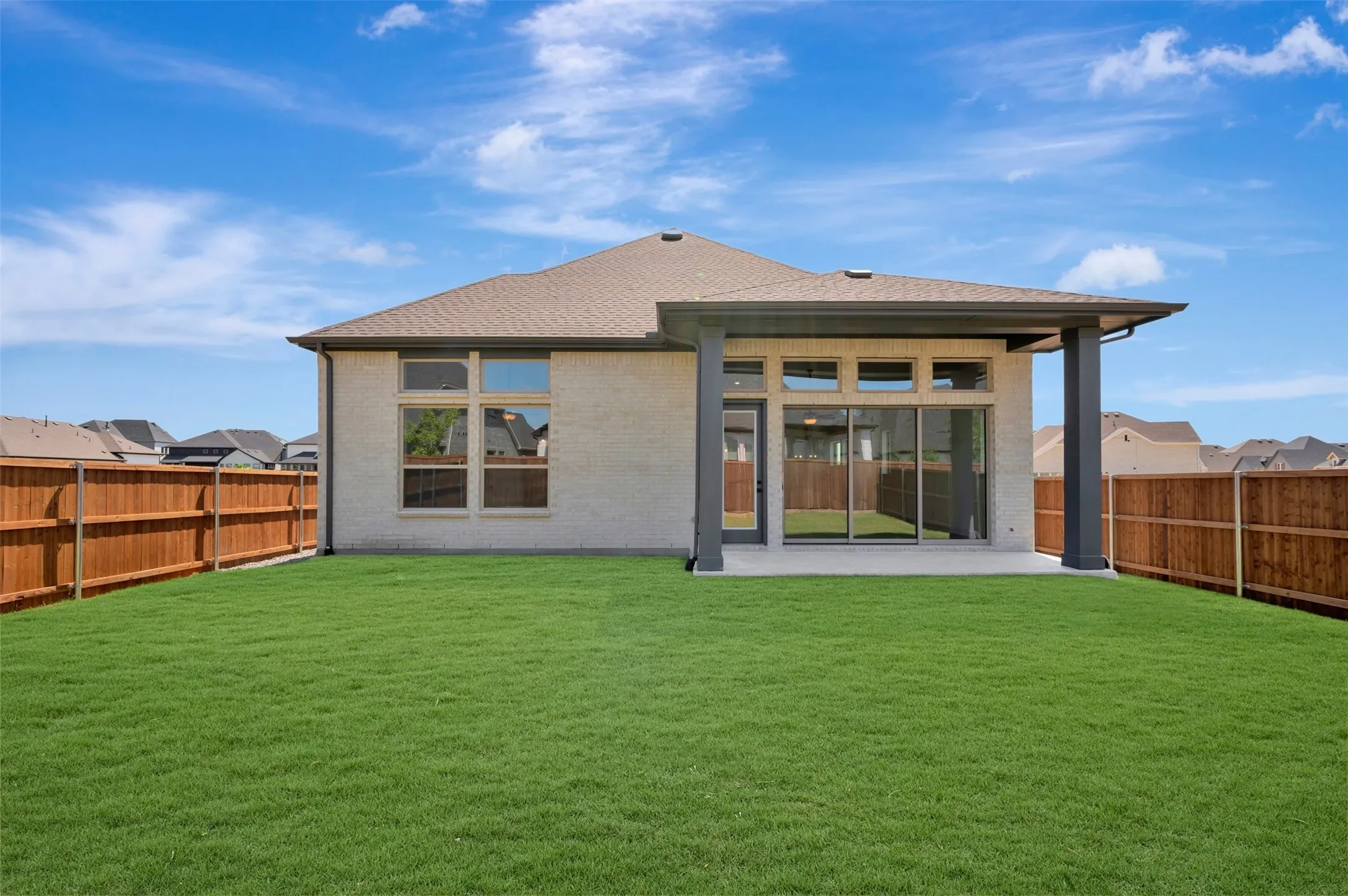Expansive backyard featuring a manicured lawn, wood fencing, and a covered patio with sliding glass doors