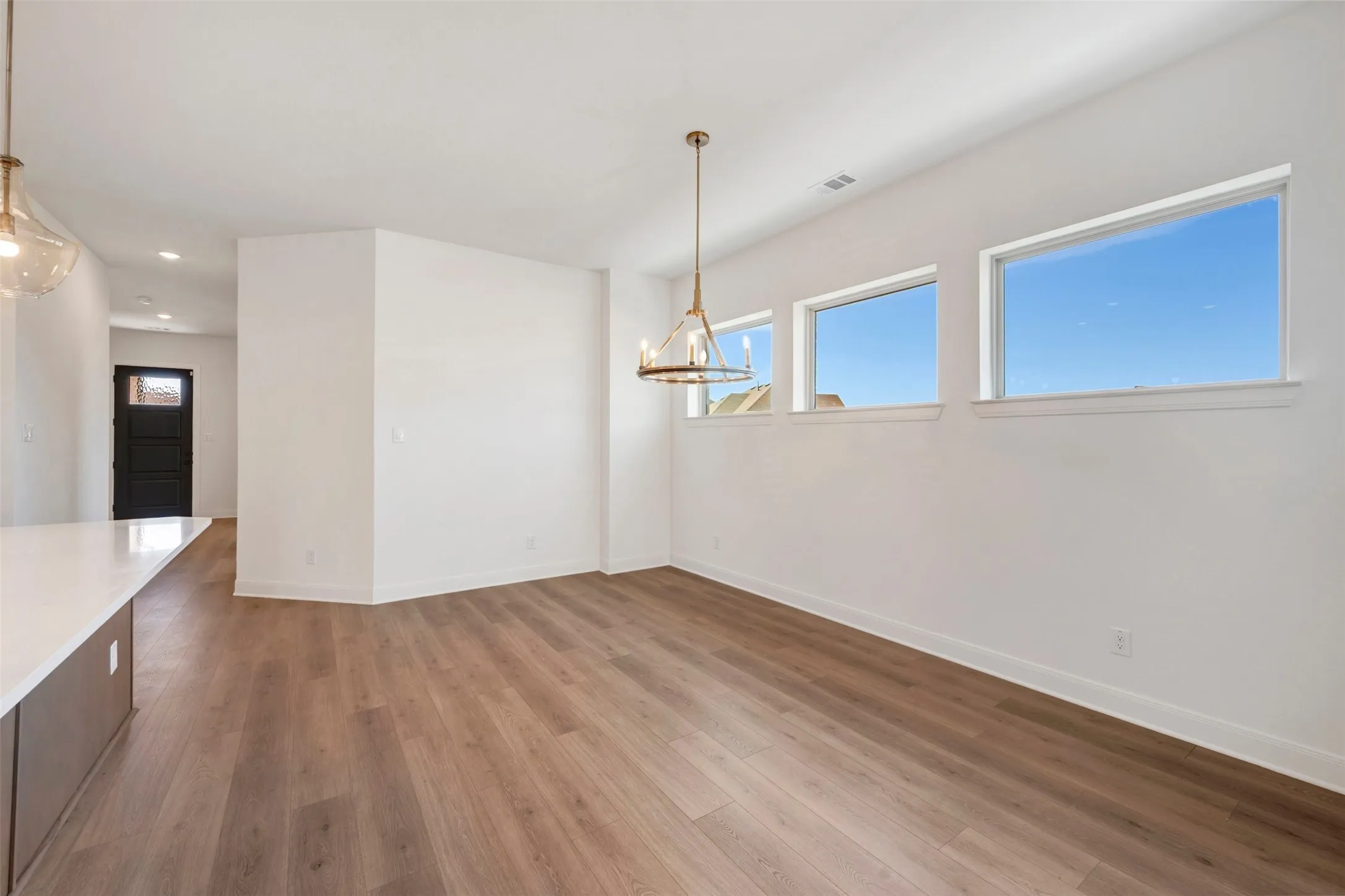 Hardwood-style flooring throughout, three horizontal windows, and a contemporary chandelier