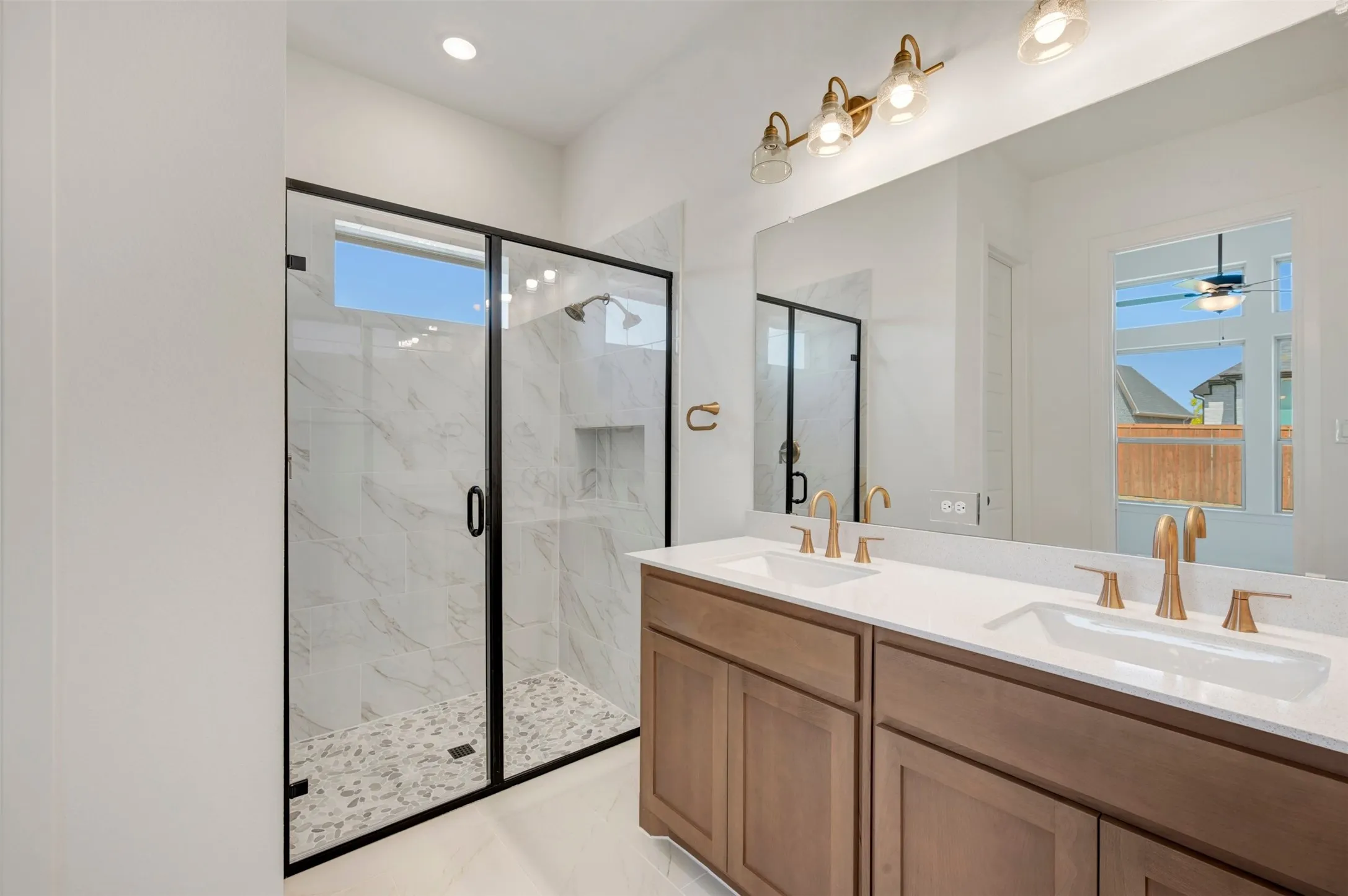 Dual vanity with light wood-finish cabinetry, quartz countertops, and brushed gold fixtures
