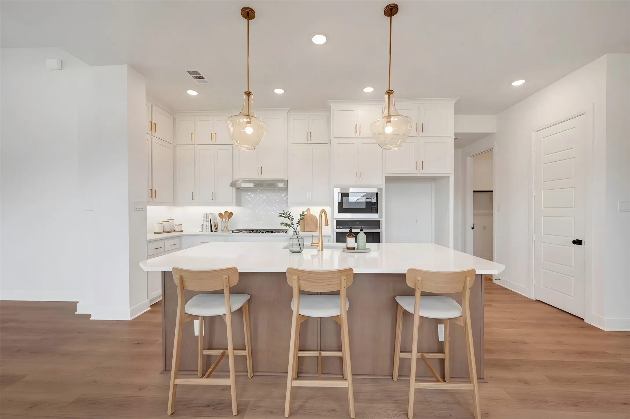 Expansive kitchen island with seating, white shaker cabinetry, stainless steel appliances, pendant lighting, and wood-finish flooring