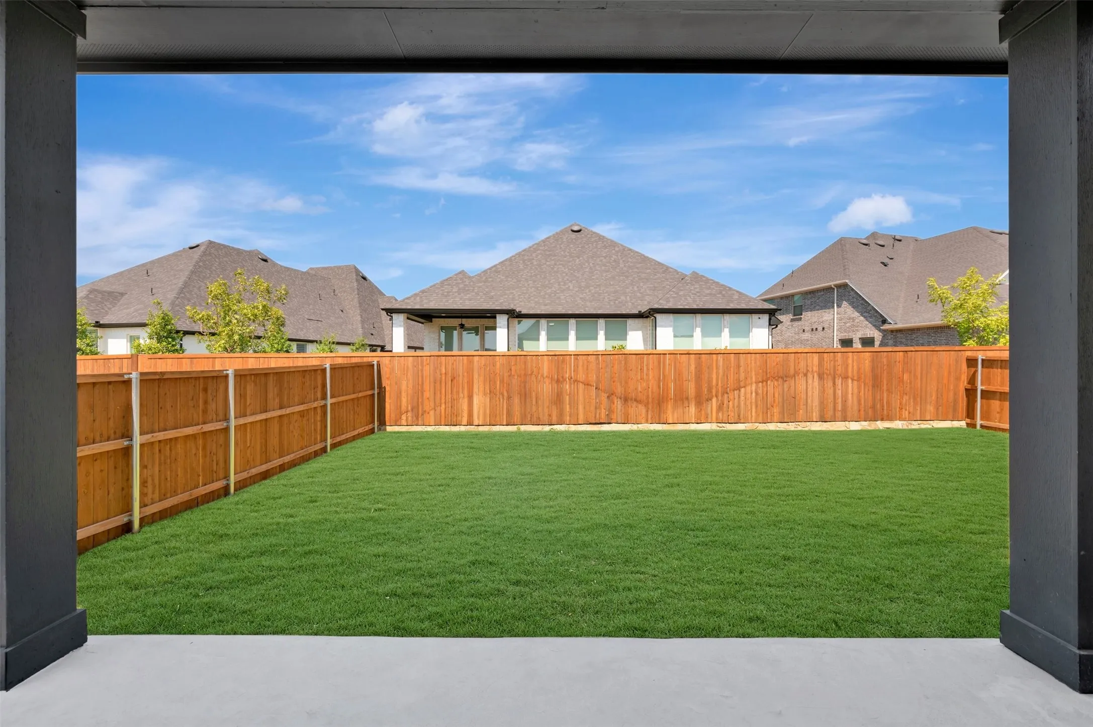 Expansive backyard featuring a manicured lawn, wood fencing, and concrete patio