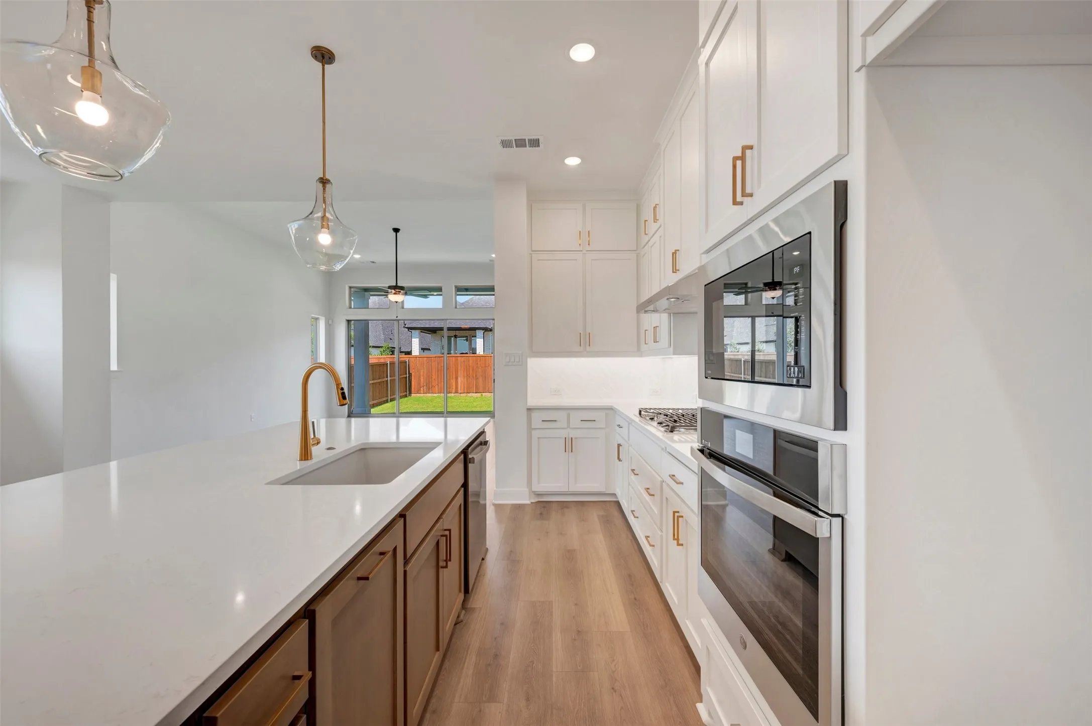Gourmet kitchen featuring a large island with an undermount sink, built-in stainless steel appliances, white cabinetry, and wood-finish flooring
