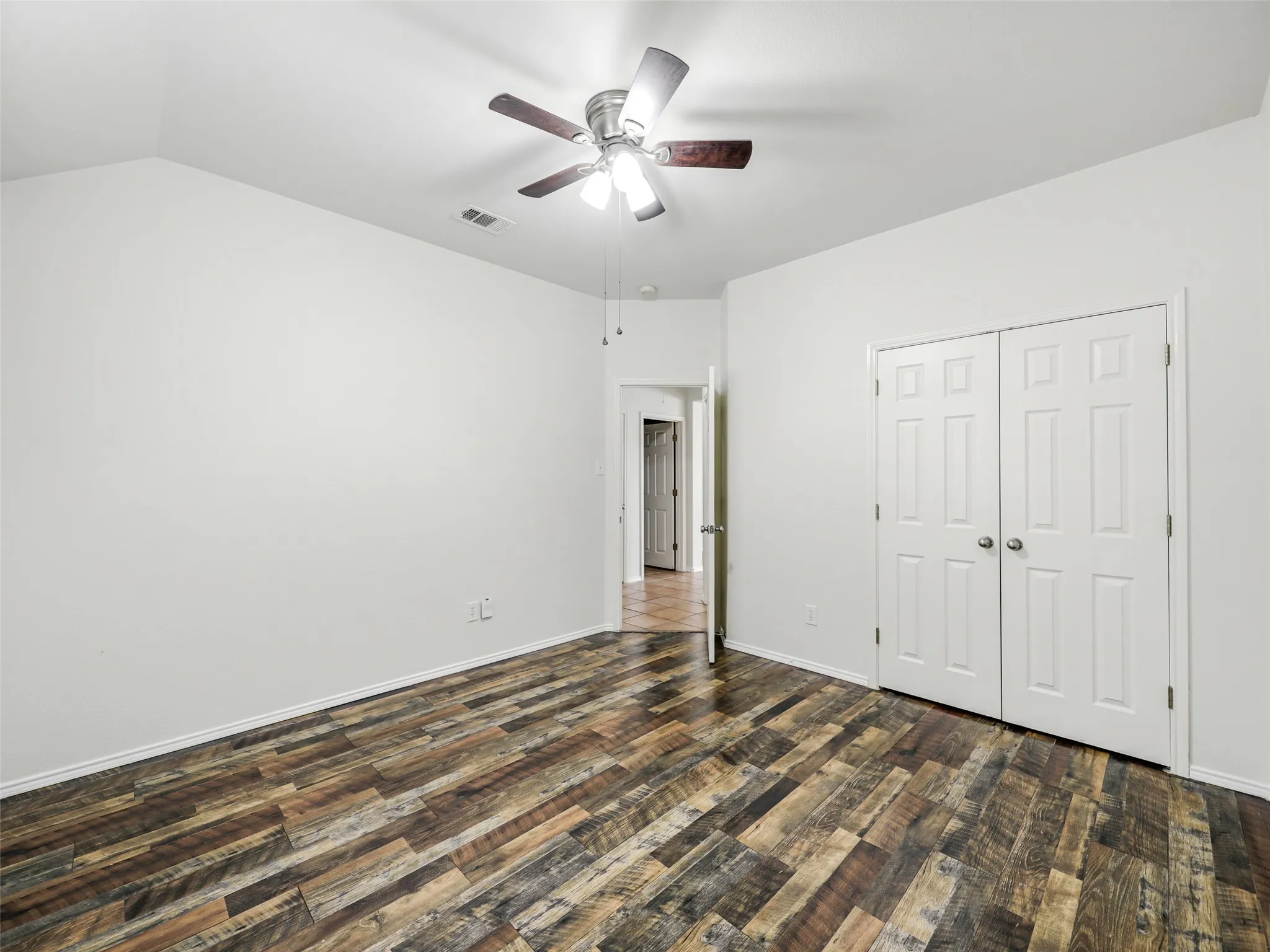 Reverse angle of the guest bedroom at 414 Dartmoor Dr, Celina, TX, showing the double-door closet and hallway entry. Highlights include cohesive multi-tone wood-look plank floors, crisp white trim and walls, and a ceiling fan with light fixture.