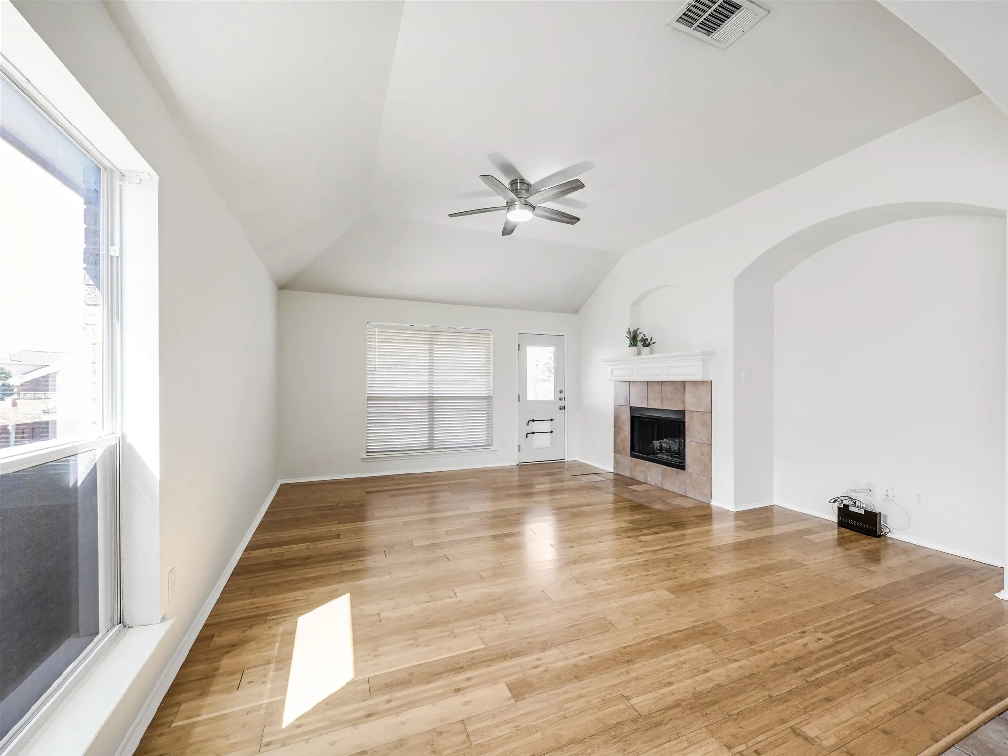 Vaulted ceiling living space featuring wood-finish flooring, a tiled fireplace with white mantle, and an arched wall opening