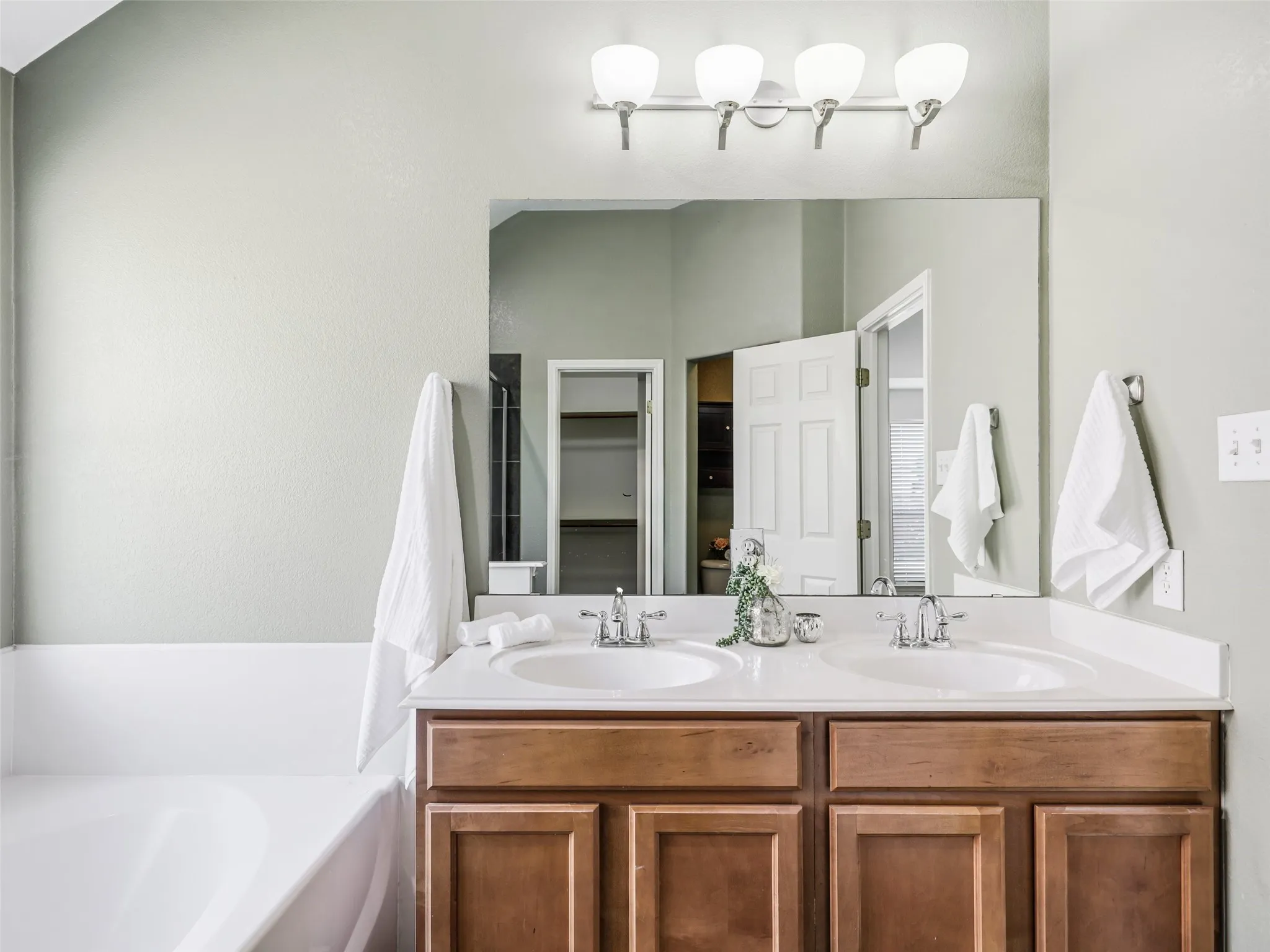 Primary ensuite bathroom at 414 Dartmoor Dr in Carter Ranch. Features a double vanity with wood cabinetry and dual undermount sinks, modern brushed nickel faucets, a wall-to-wall mirror, 4-light vanity fixture, a deep soaking garden tub.
