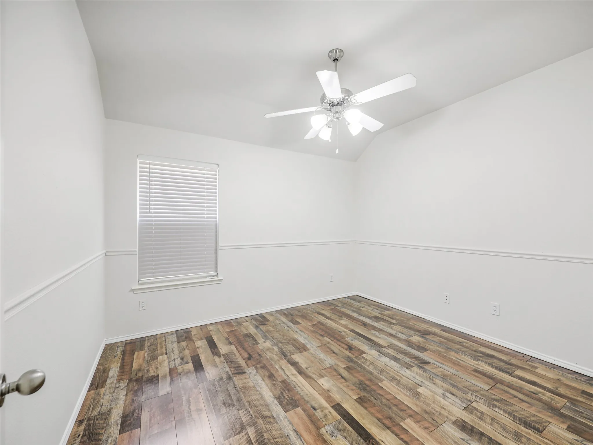 A spacious secondary bedroom at 414 Dartmoor Dr, Celina, TX. The room includes multi-tone wood-look plank flooring, detailed white chair rail trim along neutral walls, a white 5-blade ceiling fan with light kit, and a large window with 2-inch faux wood blinds for natural​​‌​​​​‌​​‌‌​‌‌​​​‌‌​‌​‌​‌​​​‌​​ light.