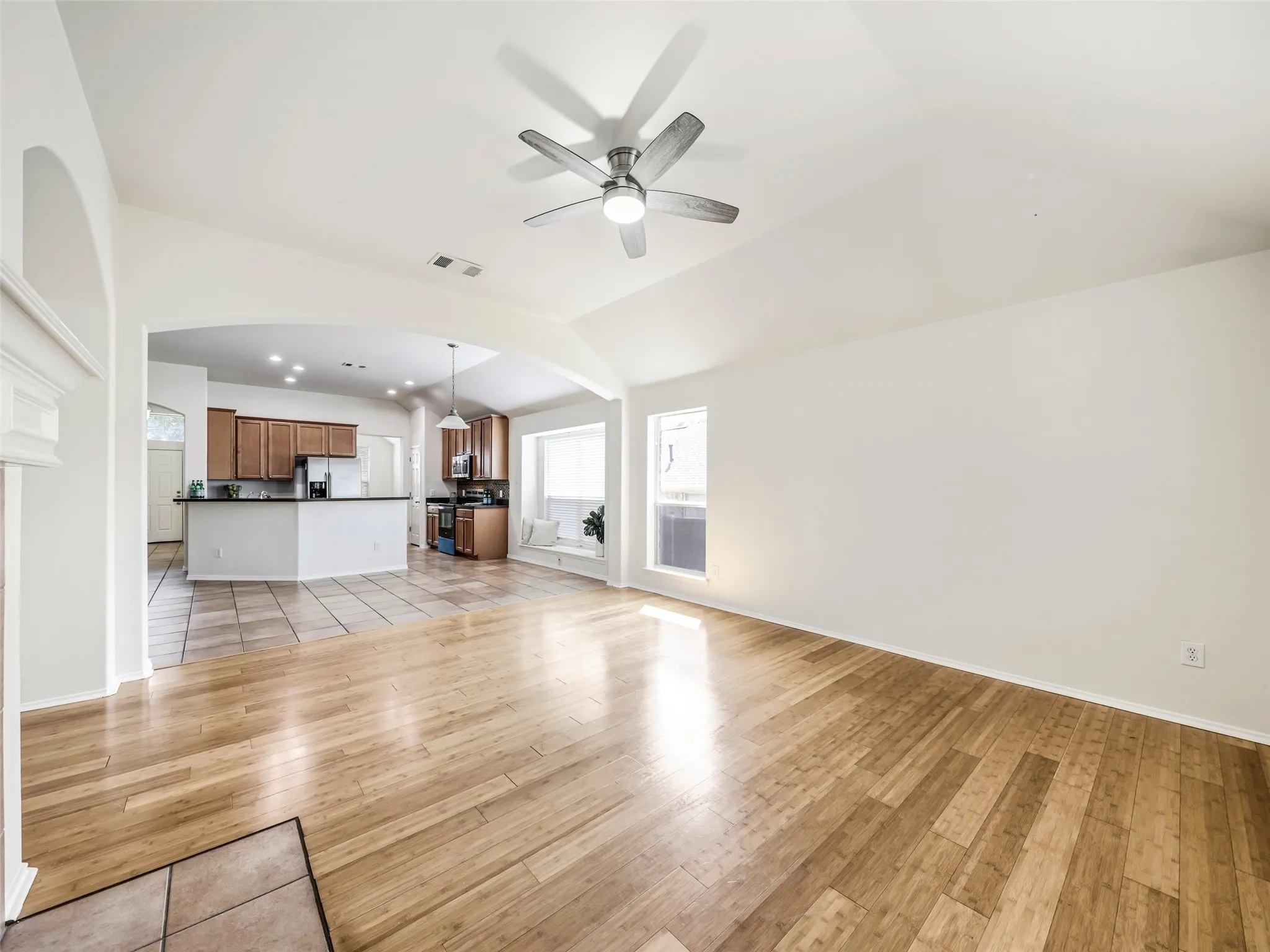Broad overview of the main family room at 414 Dartmoor Dr in Celina's Carter Ranch neighborhood. The room features high vaulted ceilings, modern wood-look plank flooring, a sleek nickel ceiling fan with light, and an open archway connecting directly to the kitchen and breakfast areas.