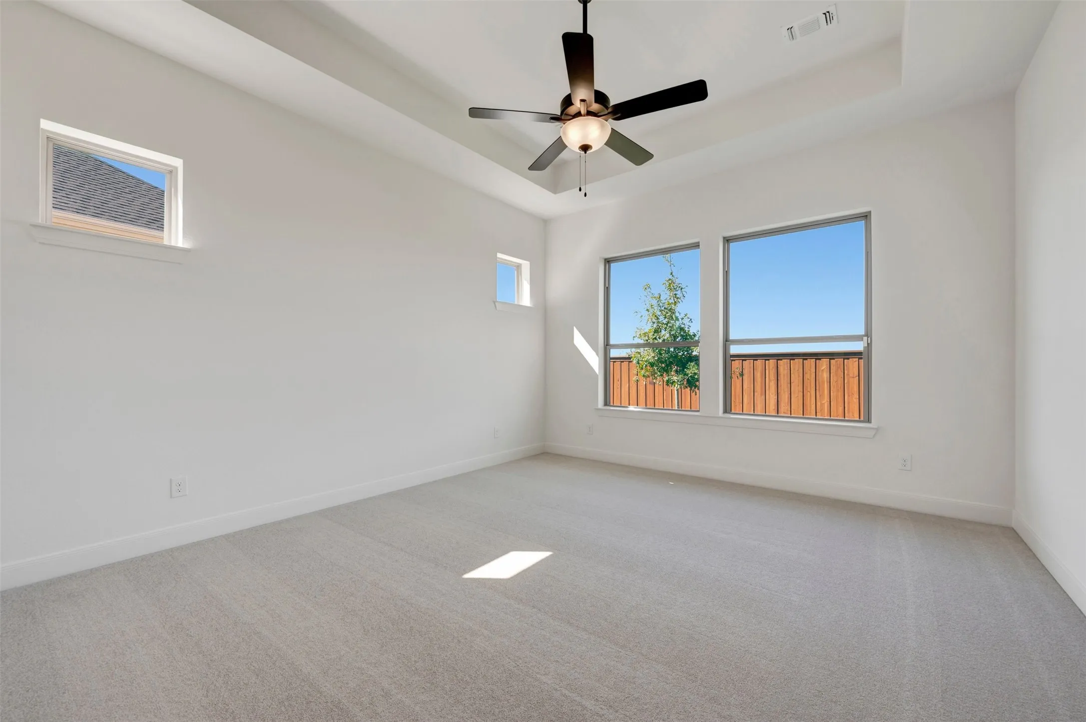 Tray ceiling with a ceiling fan, multiple windows, and light-toned carpet flooring