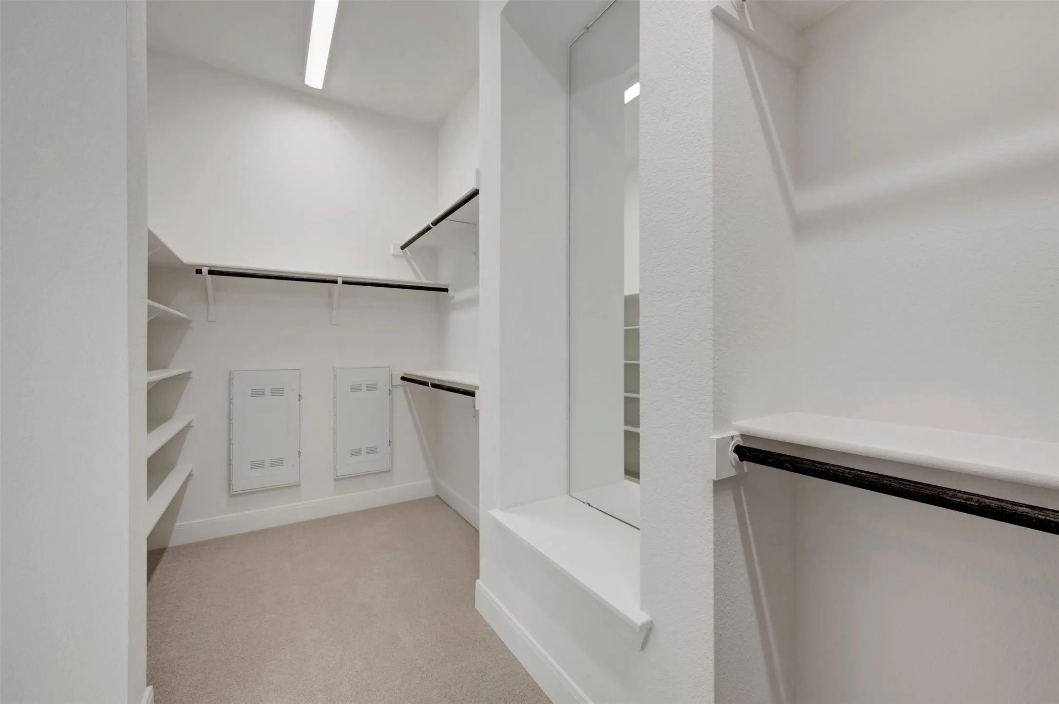 Walk-in closet with integrated shelving, multiple hanging rods, wall-mounted electrical panels, and full-length mirror
