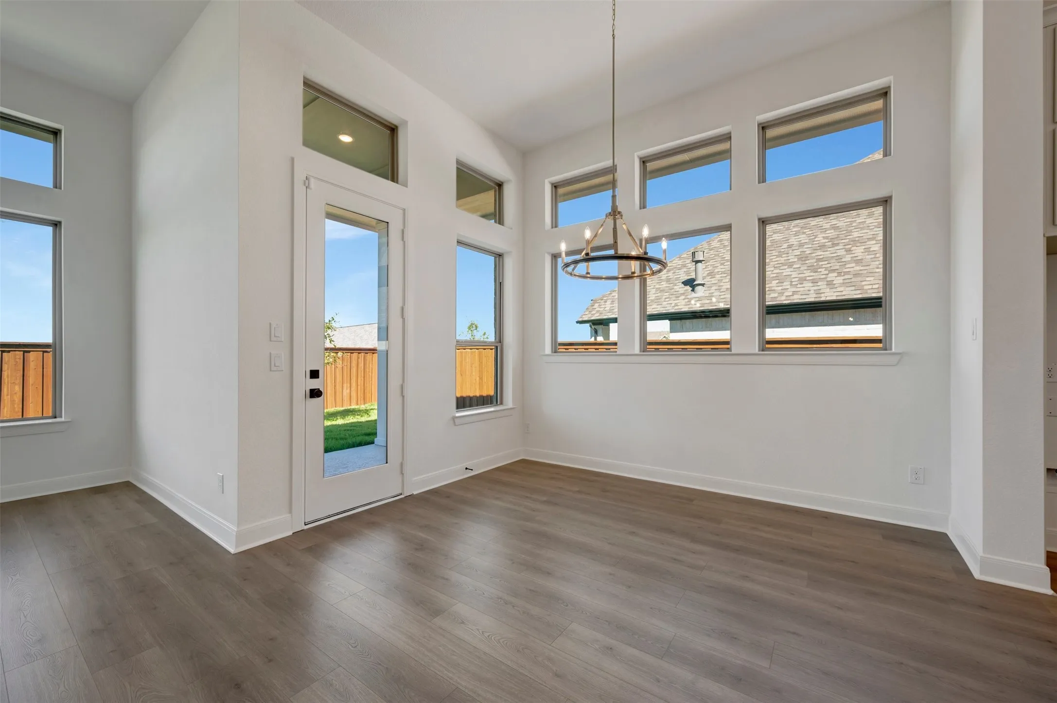 Vaulted ceiling featuring a contemporary chandelier, wood-finish flooring, and multiple windows