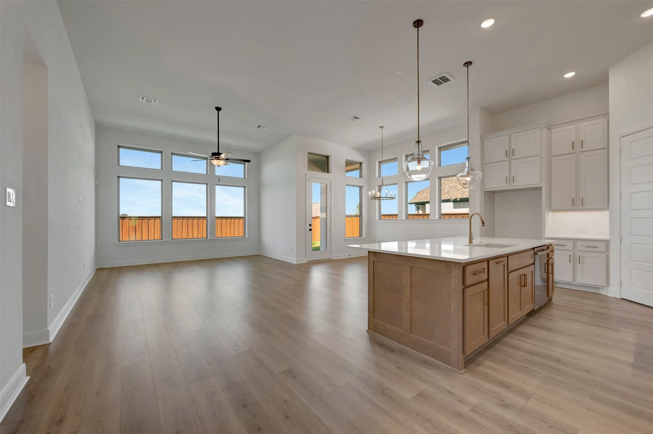 Open-concept living space with wood-finish flooring, high ceilings, multiple windows, a kitchen island with a light-colored countertop, and white cabinetry
