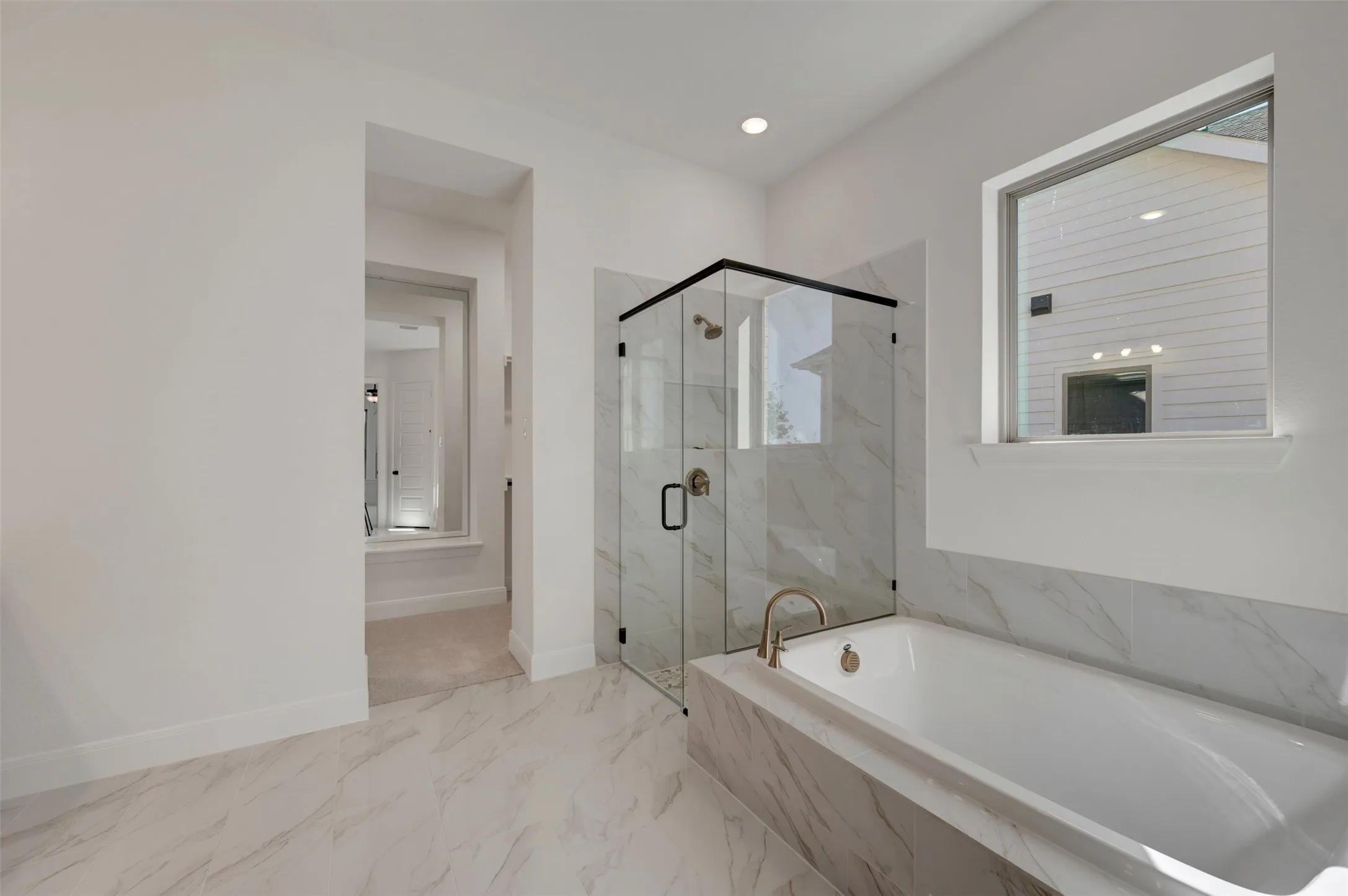 Large format tile flooring, built-in soaking tub with deck-mounted faucet, glass-enclosed shower with tile surround, recessed lighting, and a framed window