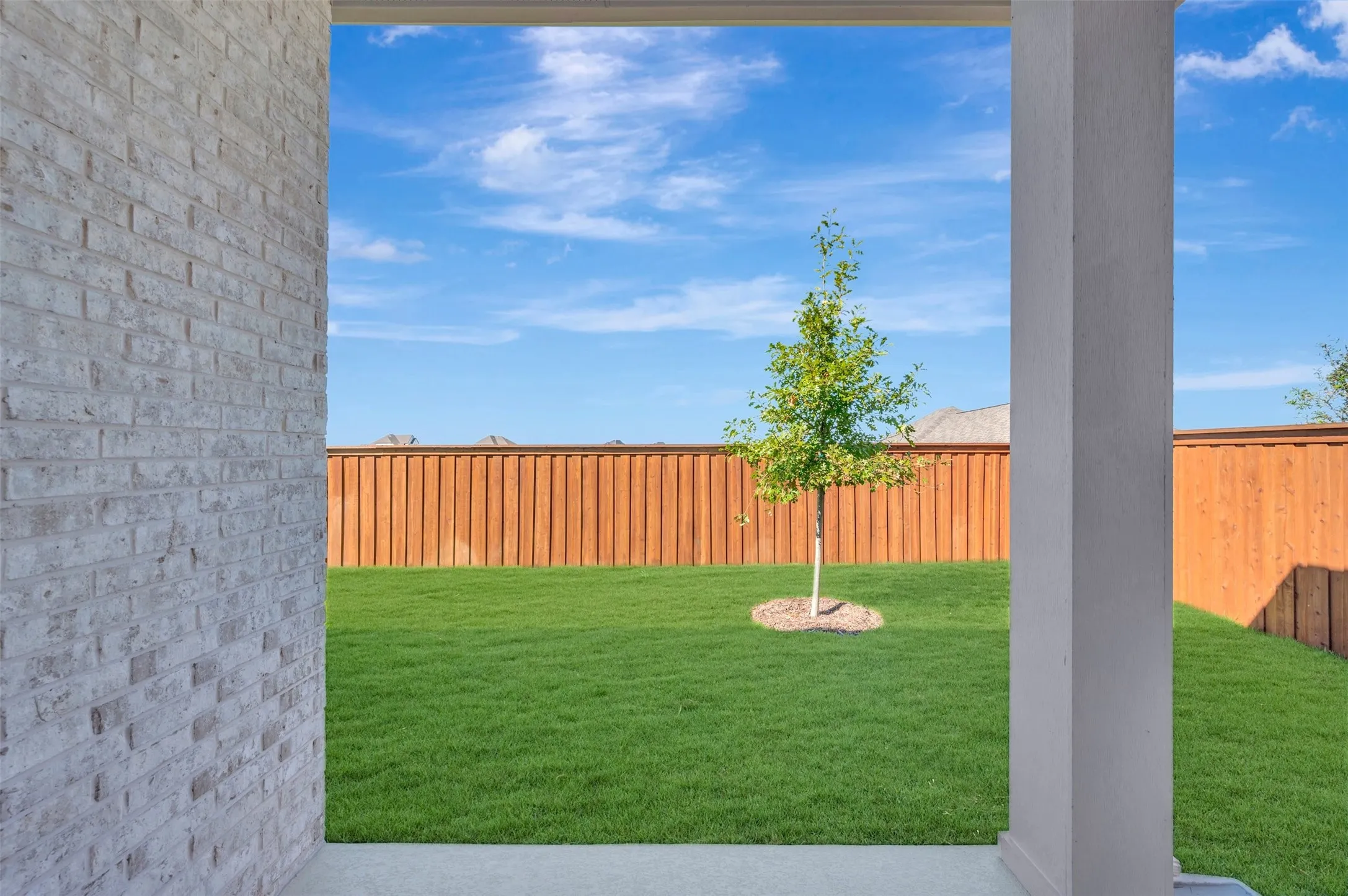 Private backyard with a manicured lawn, established tree, and wood privacy fencing
