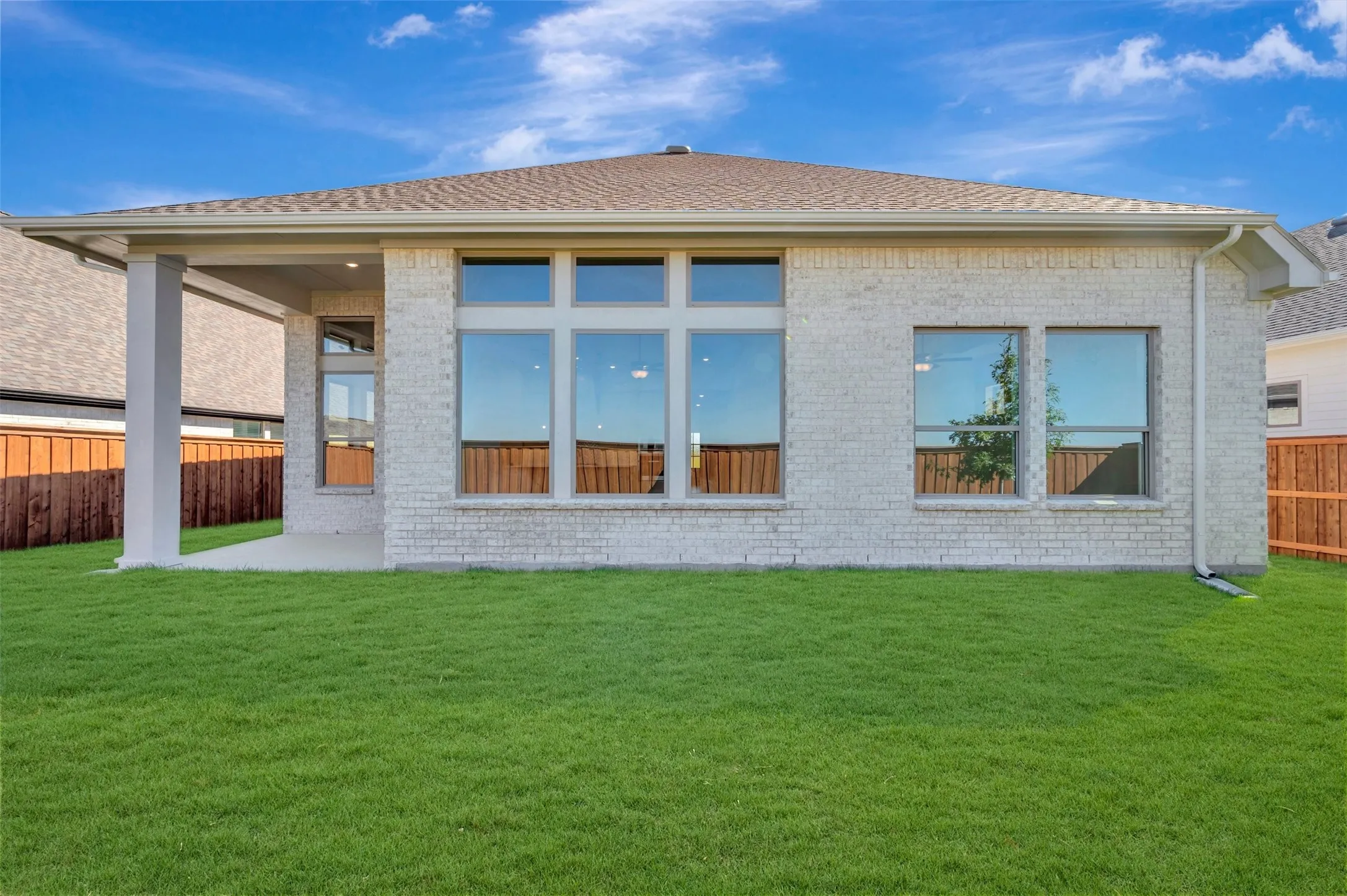 Expansive green space with a covered patio, brick exterior, large windows, and a shingle roof