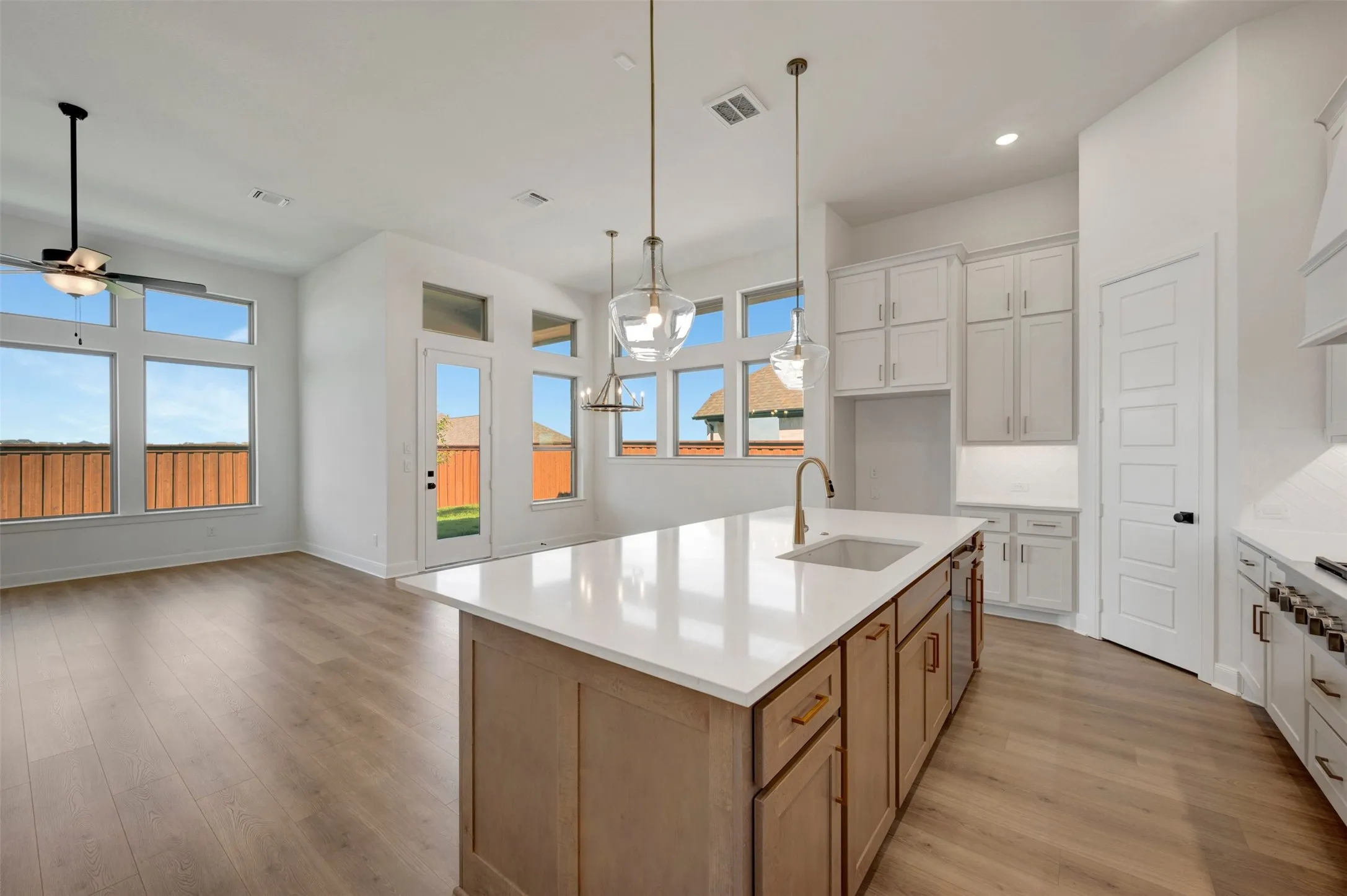Spacious kitchen featuring a large island with a composite sink and a single-handle faucet, wood-finish flooring, white cabinetry, and recessed lighting