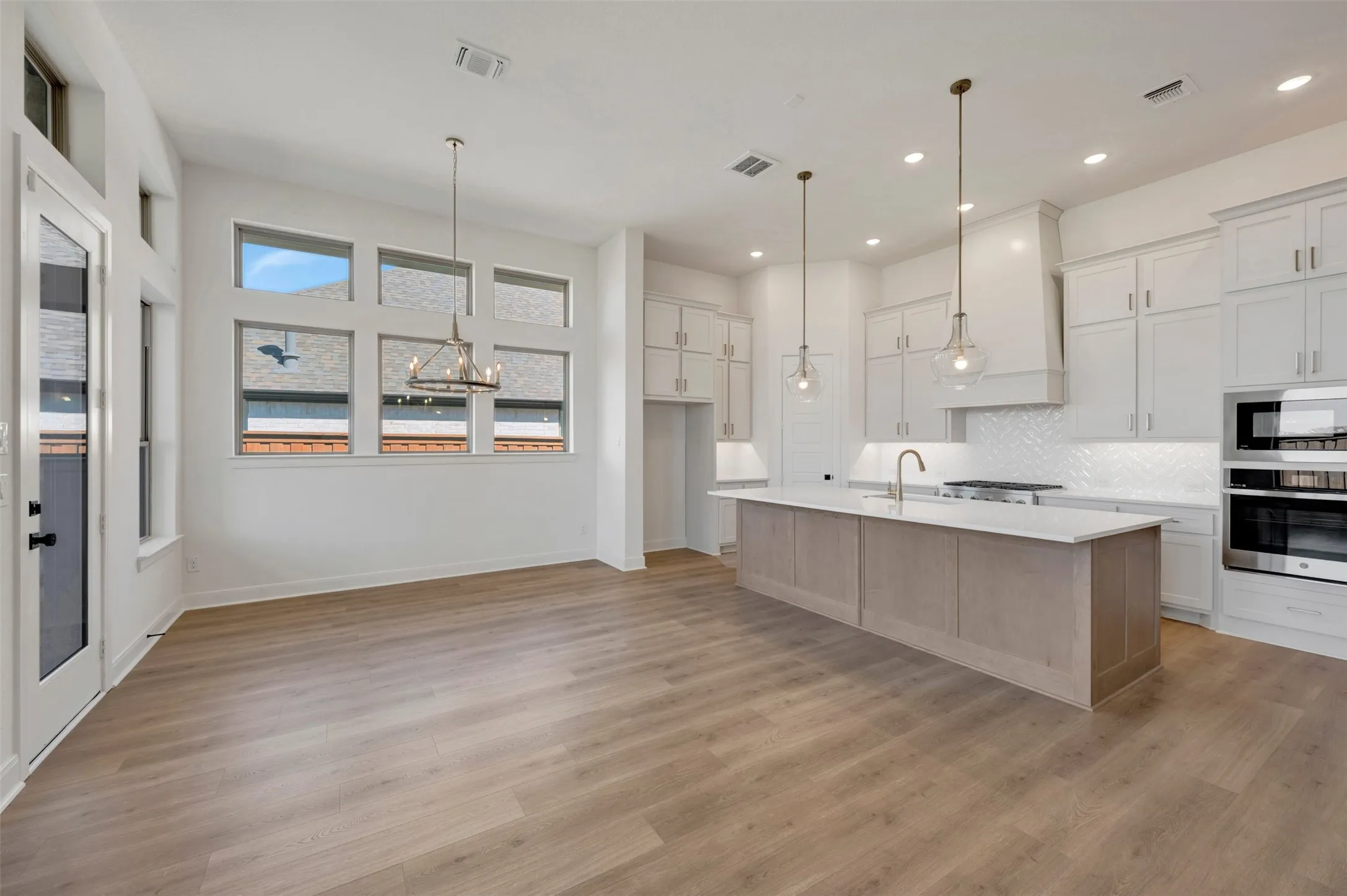 Open-concept living space with wood-finish flooring, a kitchen island, white cabinetry, a tile backsplash, and stainless steel built-in appliances