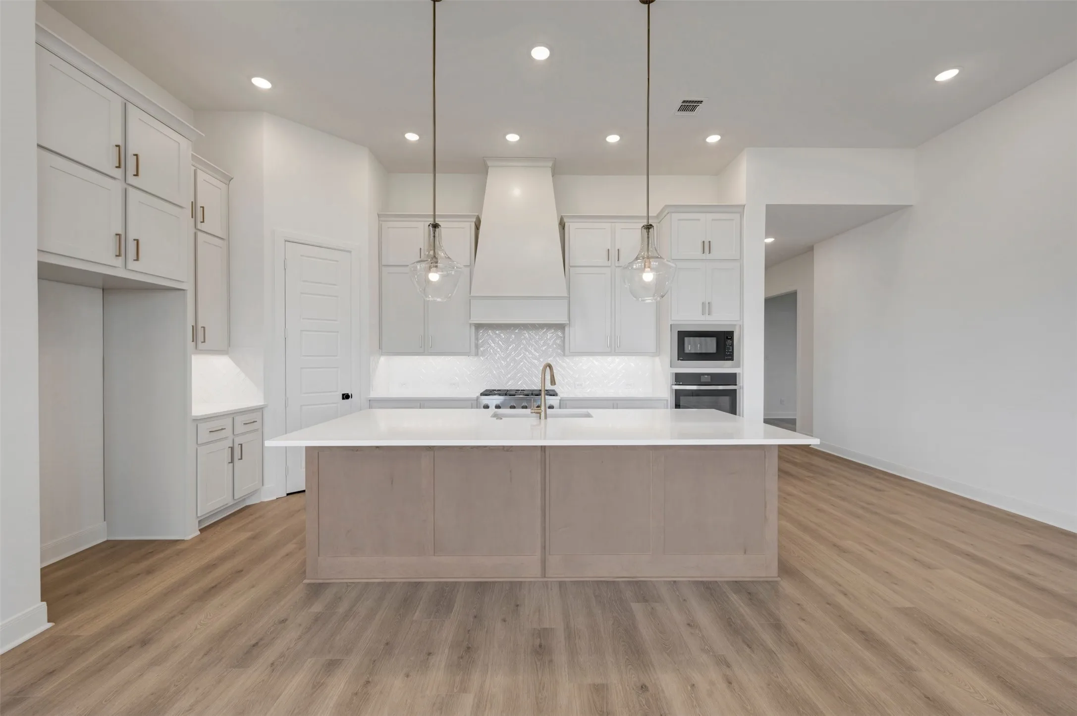 Central kitchen island with a white countertop, wood-finish flooring, recessed lighting, pendant lighting, and a white tile backsplash