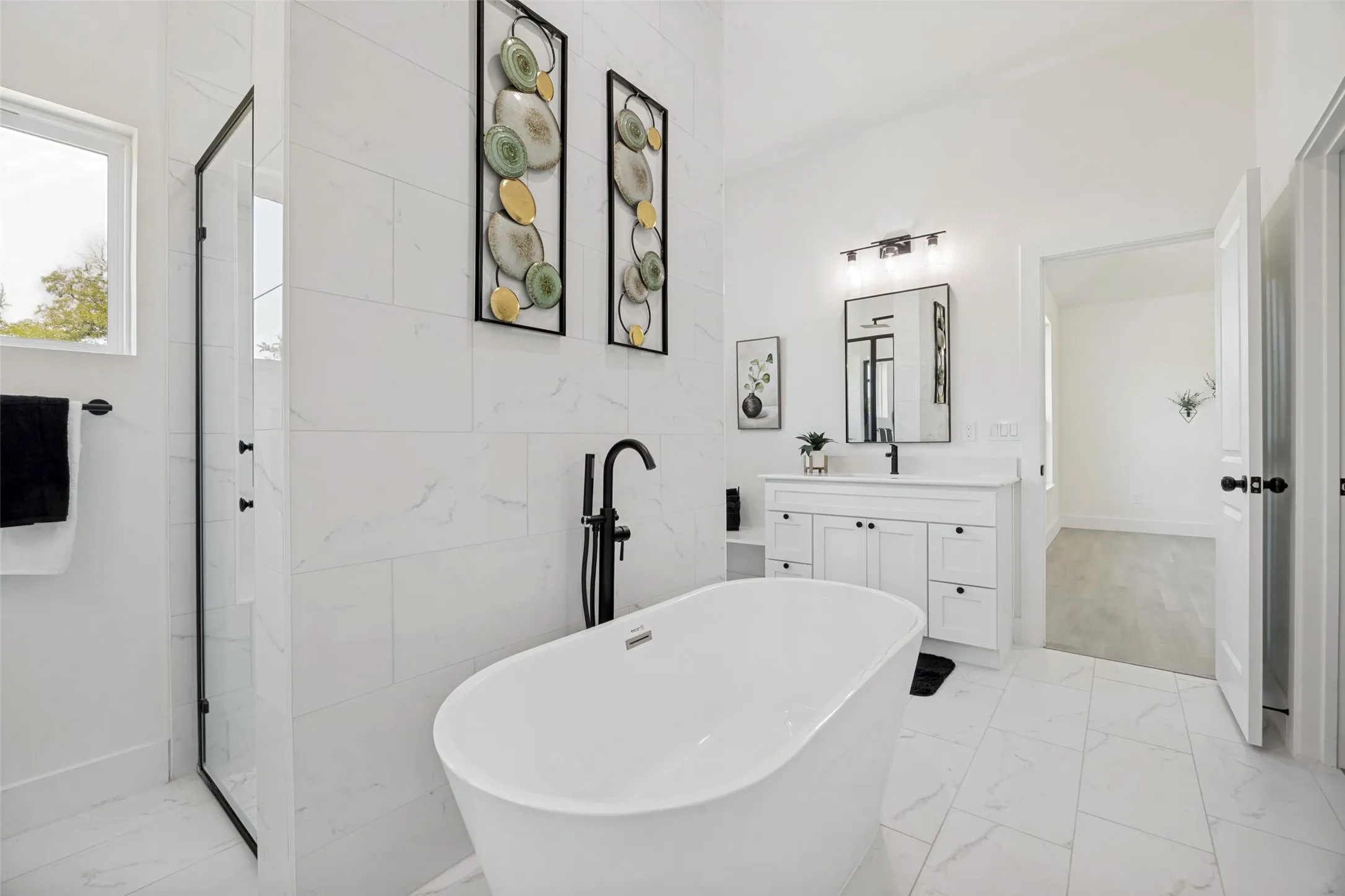 Contemporary bathroom featuring a freestanding soaking tub with a matte black floor-mounted faucet, a glass-enclosed shower with black framing, a white vanity with a rectangular sink, and large format marble-look tile flooring