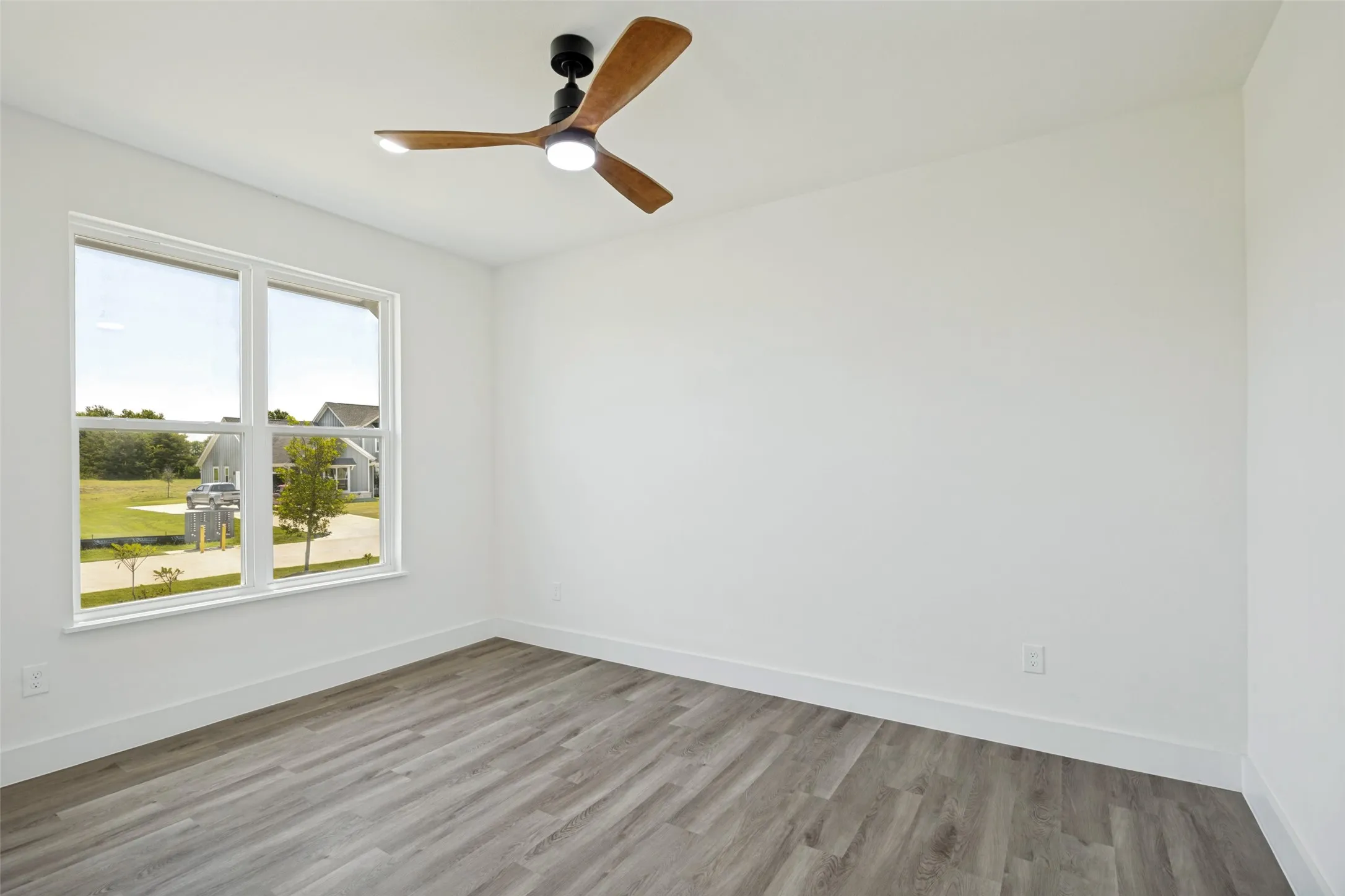 Spacious room featuring wood-finish flooring, white baseboards, and a large window