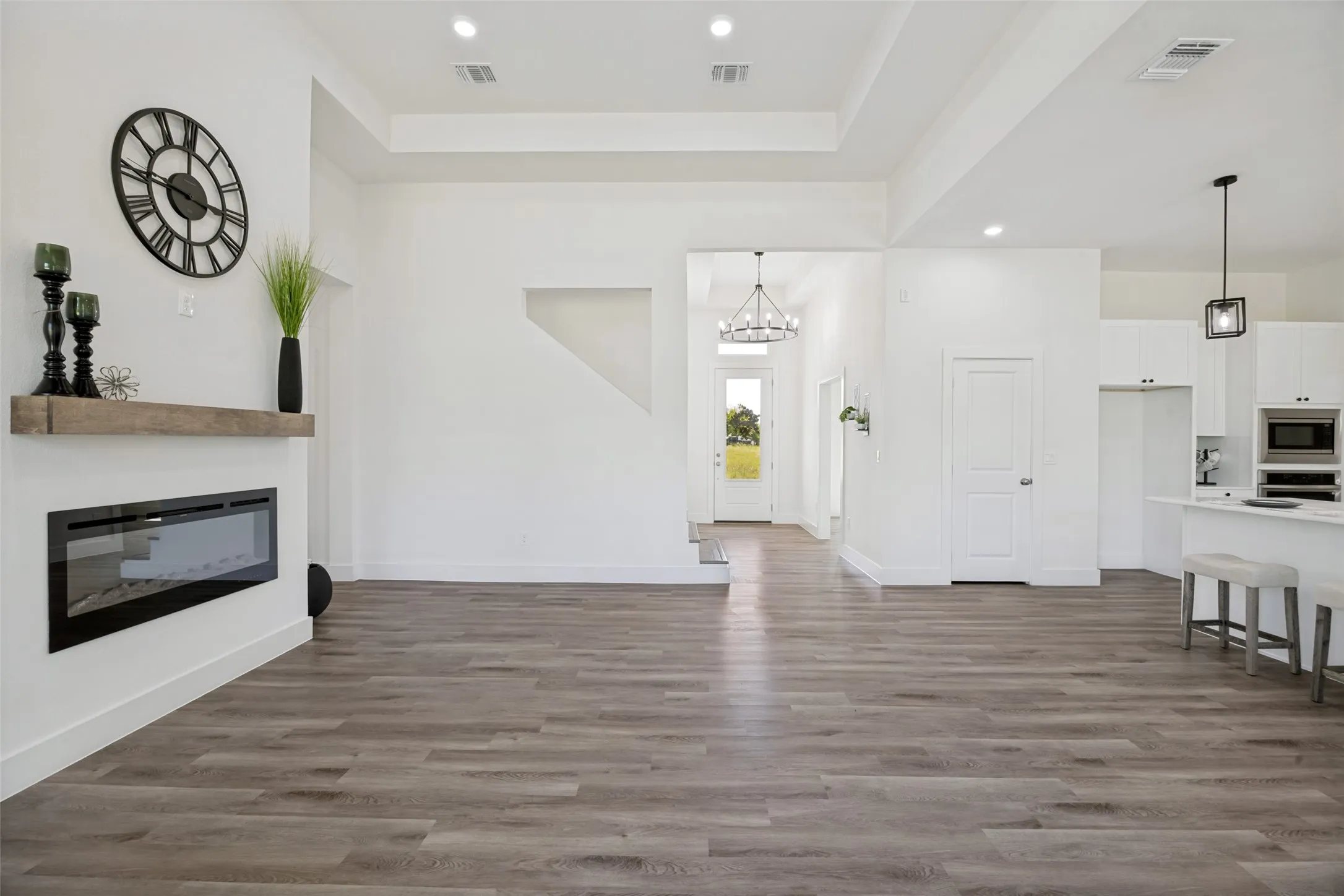 Open-concept living space featuring wood-finish flooring, a built-in fireplace with a floating wood mantle, and recessed lighting