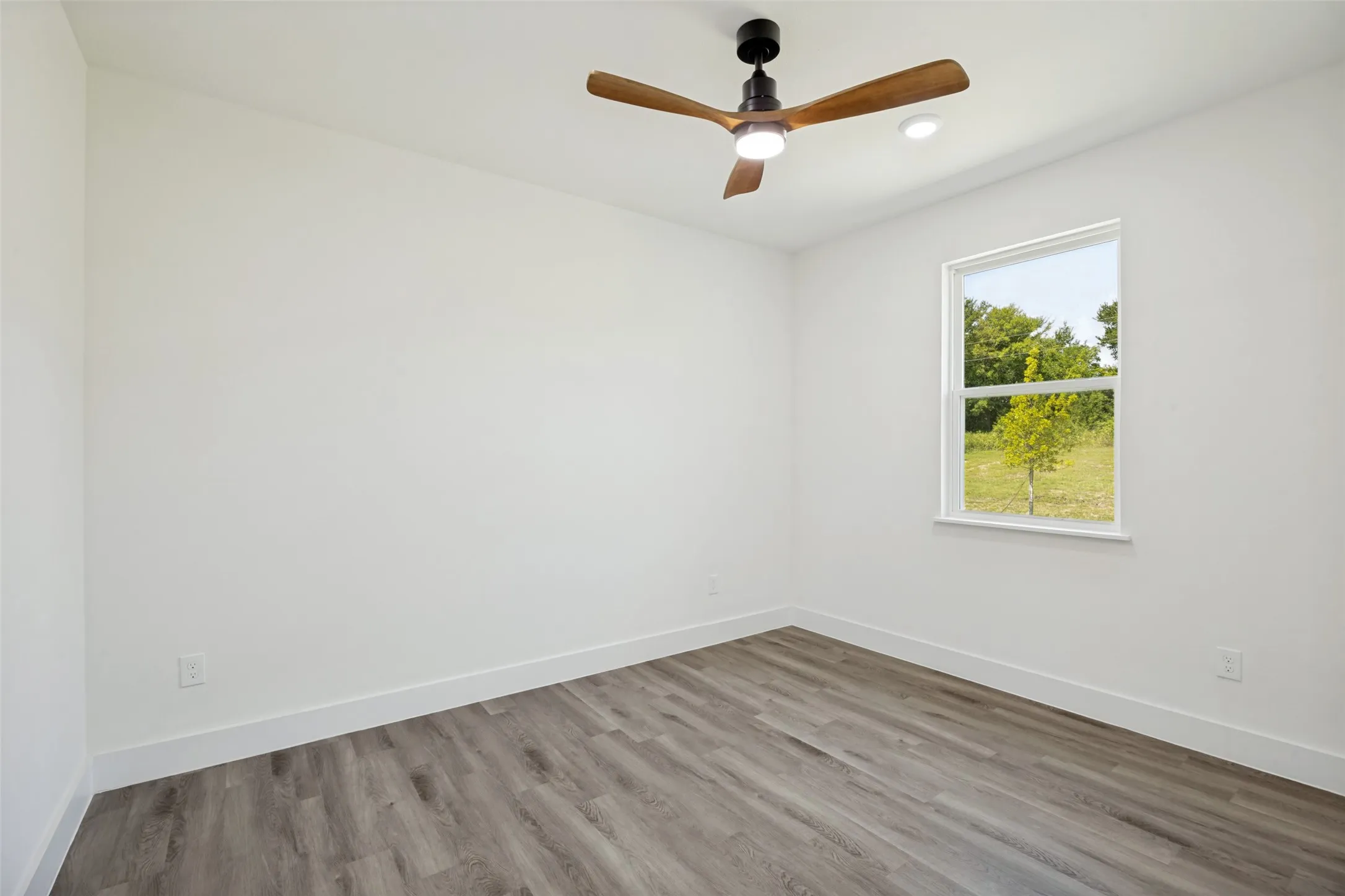 Spacious room featuring wood-finish flooring, a contemporary ceiling fan, and recessed lighting