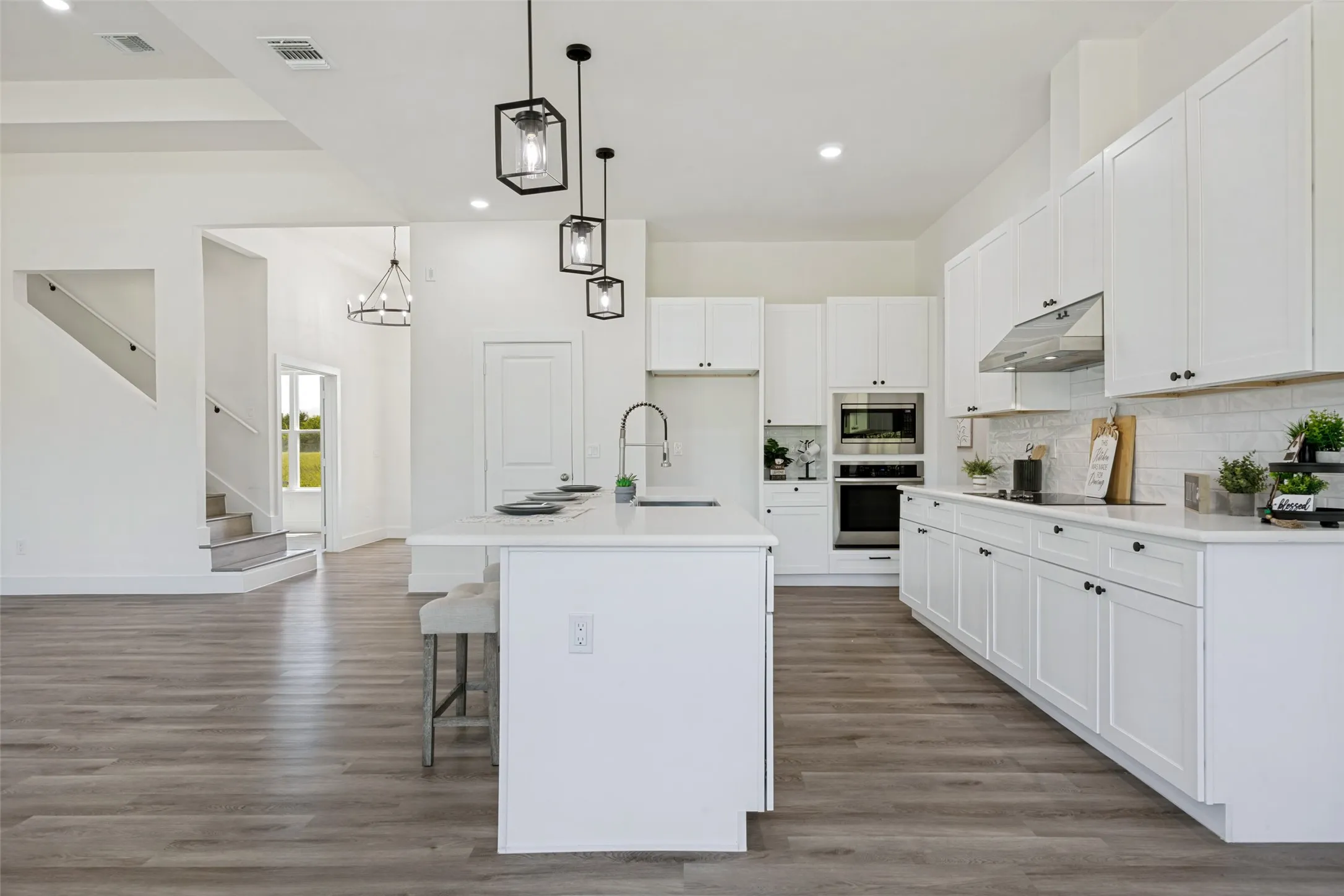 Modern kitchen featuring a large central island, white shaker cabinetry, stainless steel appliances, a tile backsplash, and wood-finish flooring