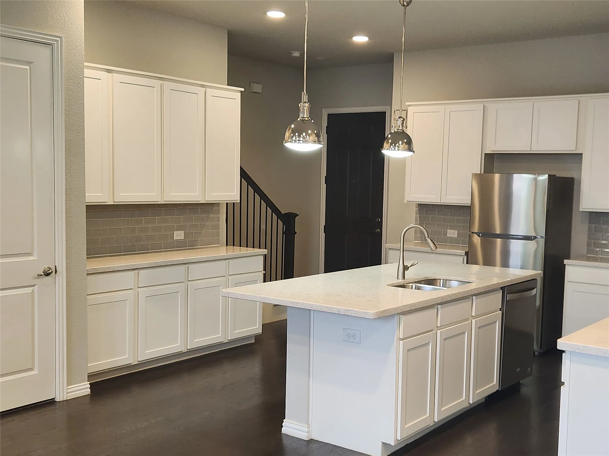 Open-concept kitchen featuring white shaker cabinetry, light-toned countertops, and a gray subway tile backsplash