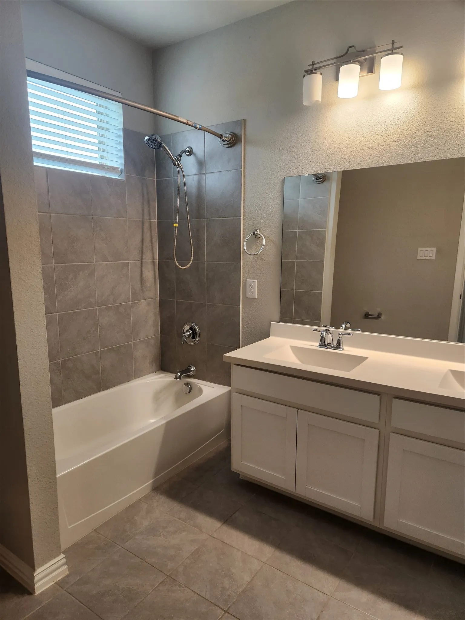 Bathroom featuring a white vanity with dual sinks, a large mirror, and a three-light fixture