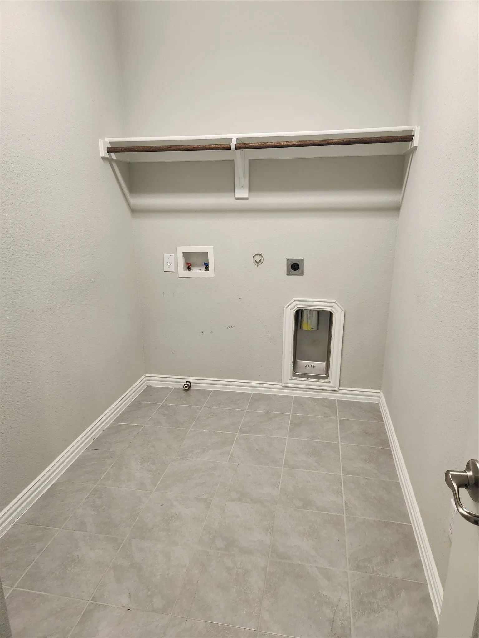 Dedicated utility room featuring tile flooring, white baseboards, and a built-in shelf with a hanging rod