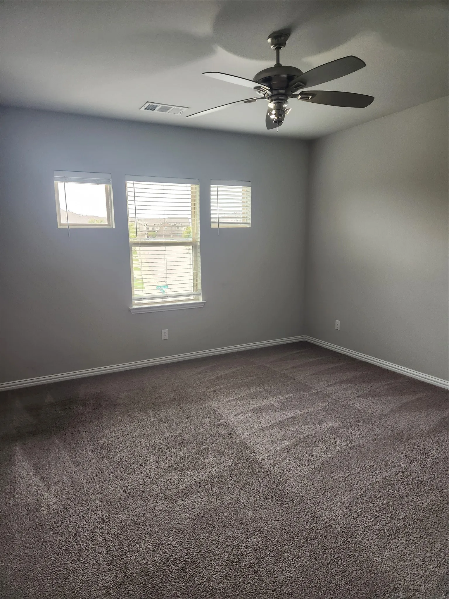 Spacious room featuring neutral carpeting, light gray walls, white trim, and a ceiling fan with integrated lighting