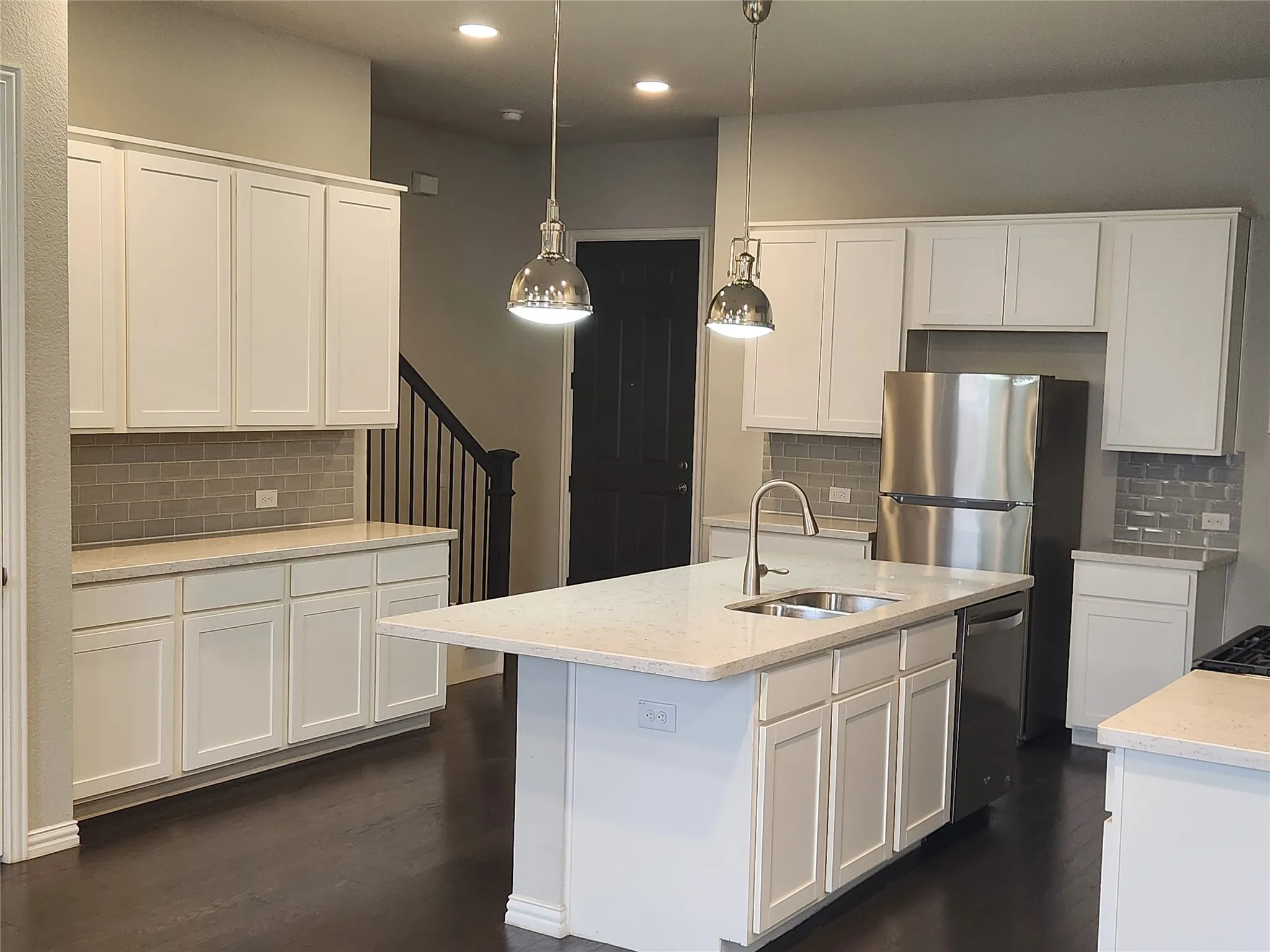 Modern kitchen featuring white shaker cabinetry, light-toned countertops, a subway tile backsplash, and dark wood-finish flooring