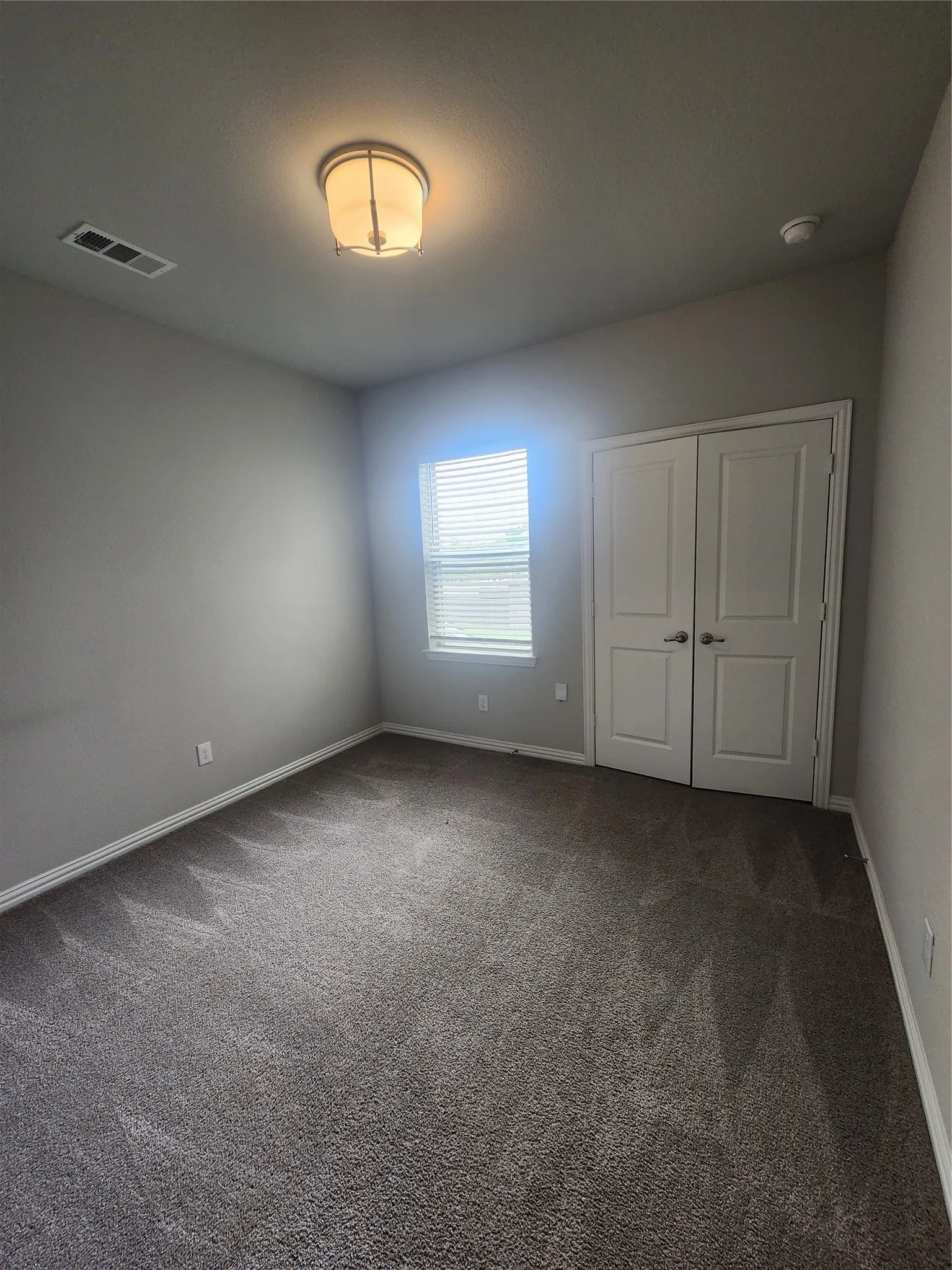 Neutral-toned room featuring a flush-mount ceiling light fixture, a window with horizontal blinds, and carpeted flooring