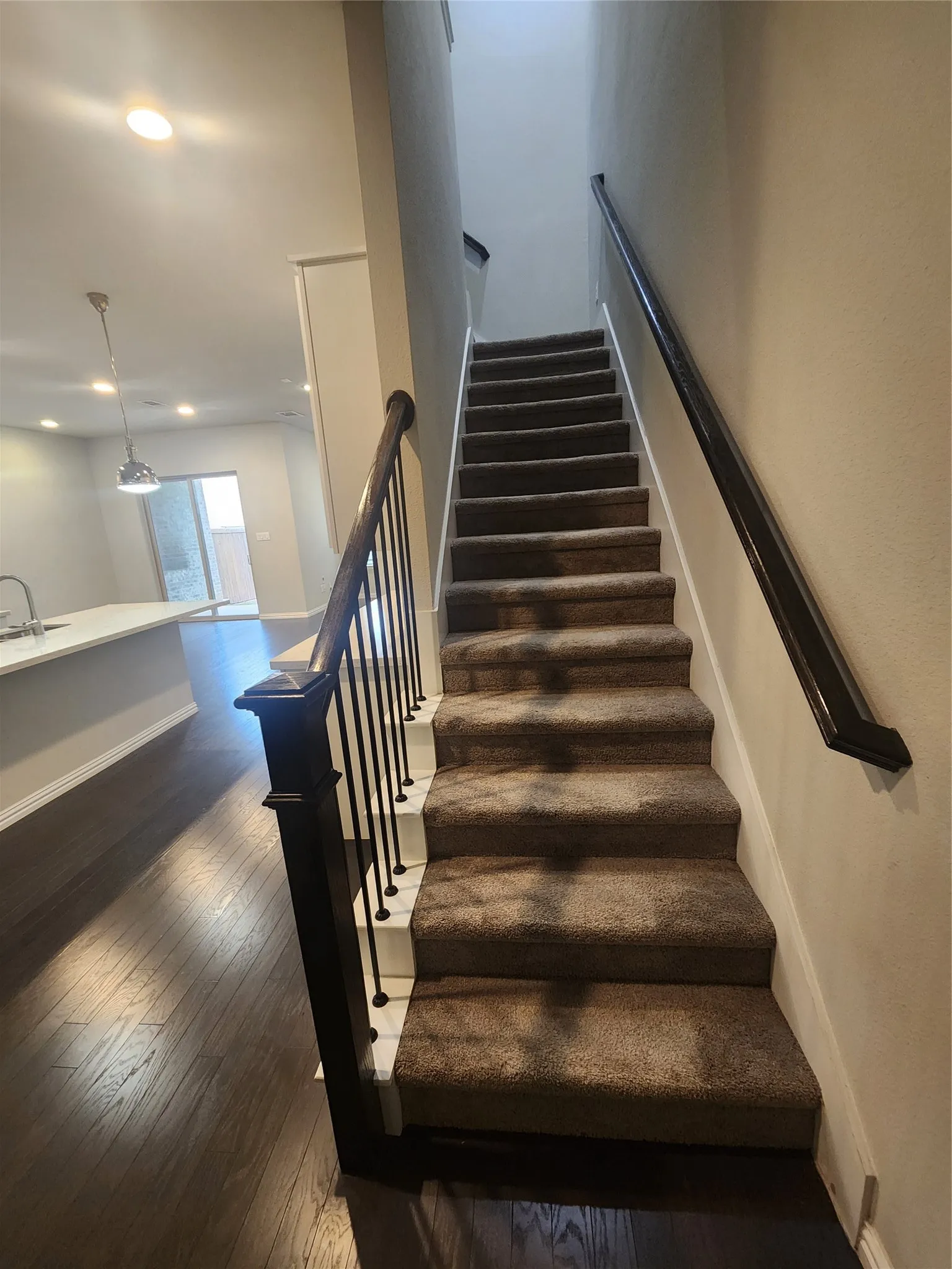 Carpeted staircase featuring black metal balusters and dark wood handrails