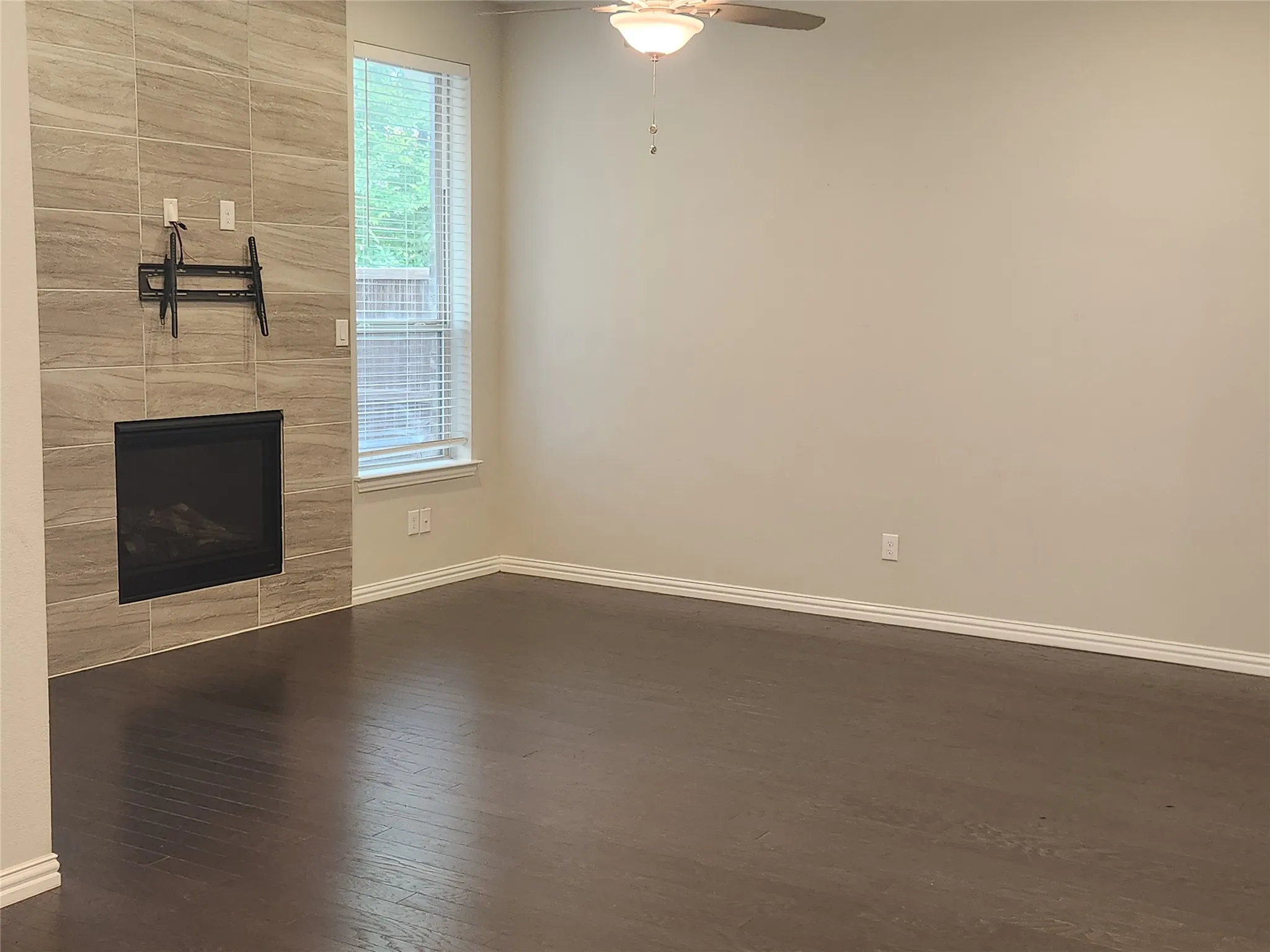 Living area featuring wood-finish flooring, a contemporary fireplace with a tile surround, a window with horizontal blinds, and a ceiling fan with integrated lighting