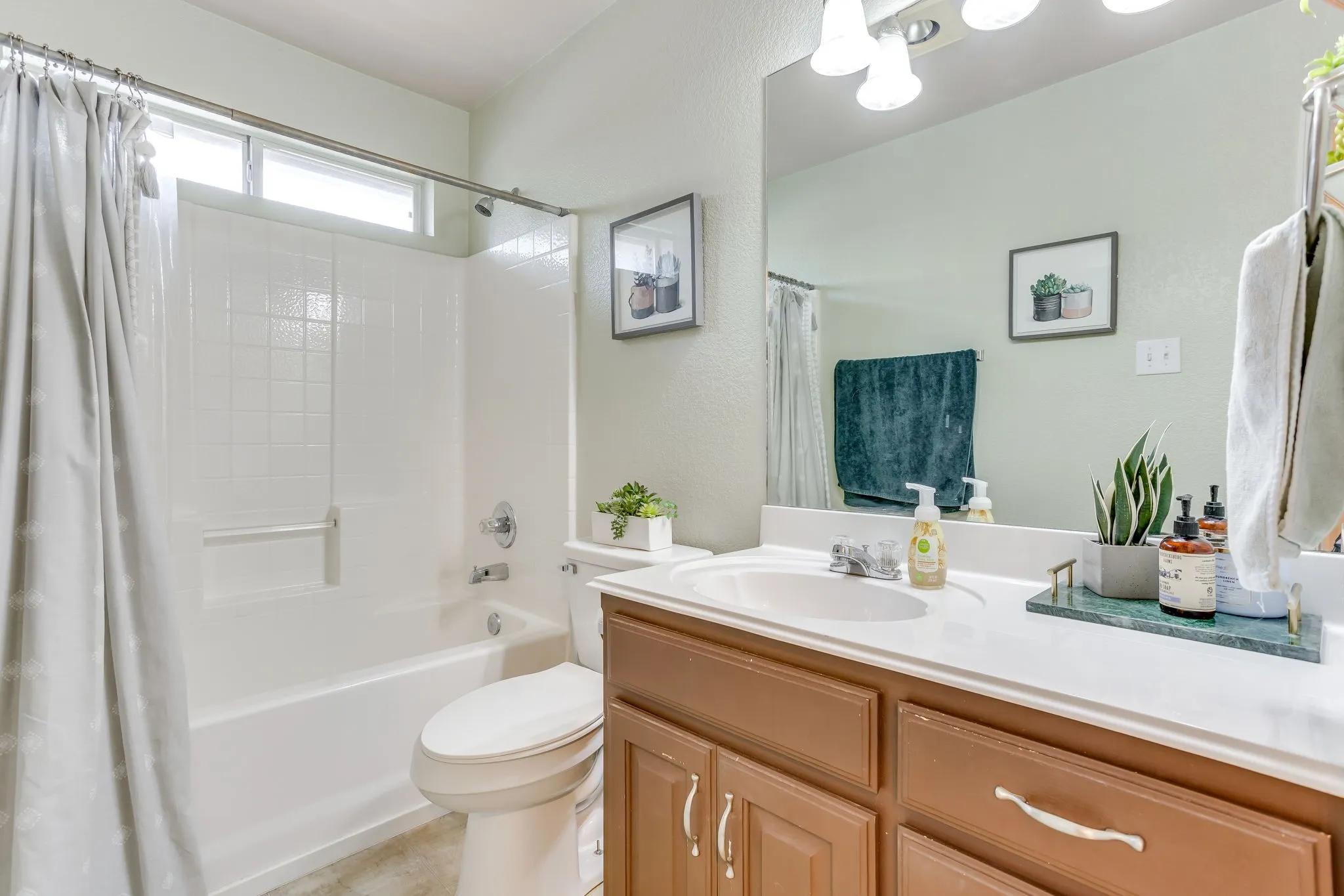 Bathroom featuring warm brown wood cabinets, solid white surface material, and a tub/shower combination with horizontal transom windows.