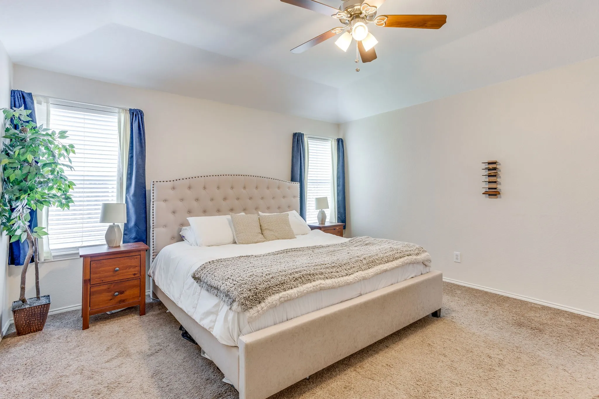 Primary bedroom featuring a recessed tray ceiling that adds vertical depth to the space, a central wooden ceiling fan with integrated light fixtured, and two windows providing ample natural light.