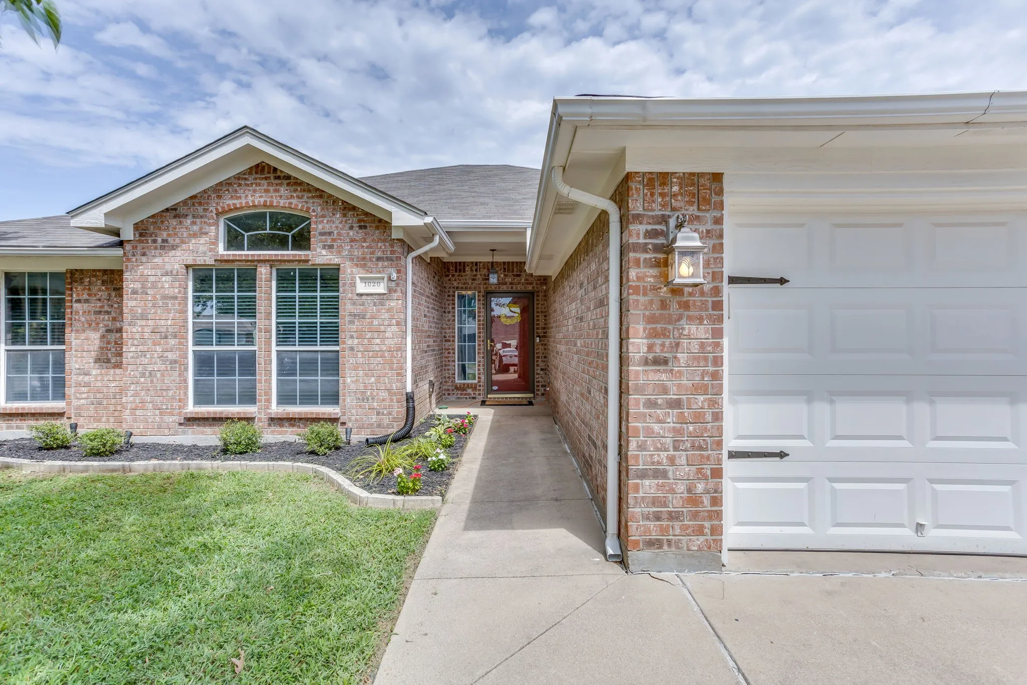 Front entry features multi-colored brick, vertical brick detailing above the main windows as an accent header, and black decorative carriage-house style accents on the garage door.