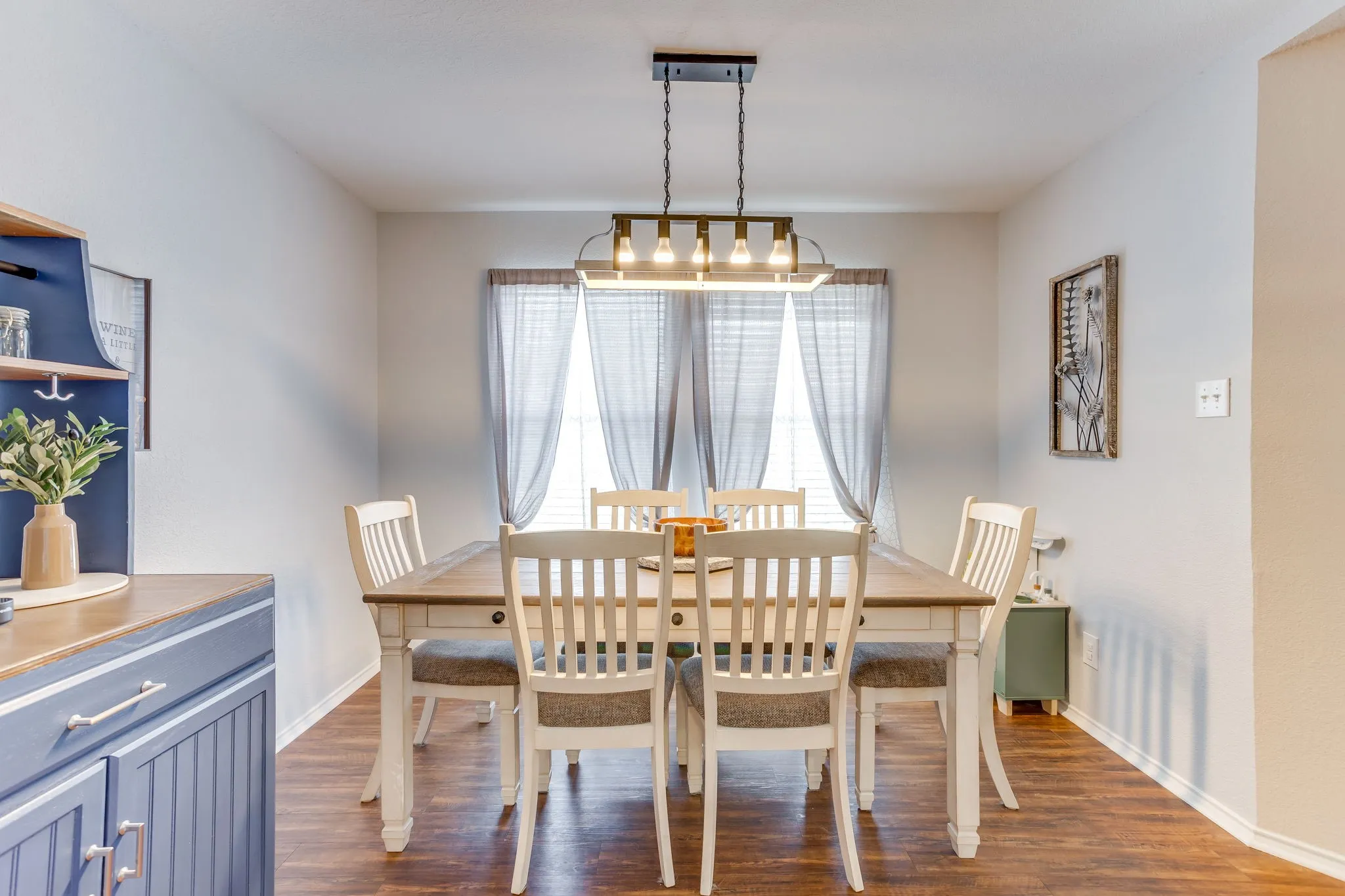 Dining area featuring neutral toned paint, medium-toned wood-style flooring, and multi-light linear fixture, and large vertical windows for abundant natural light.