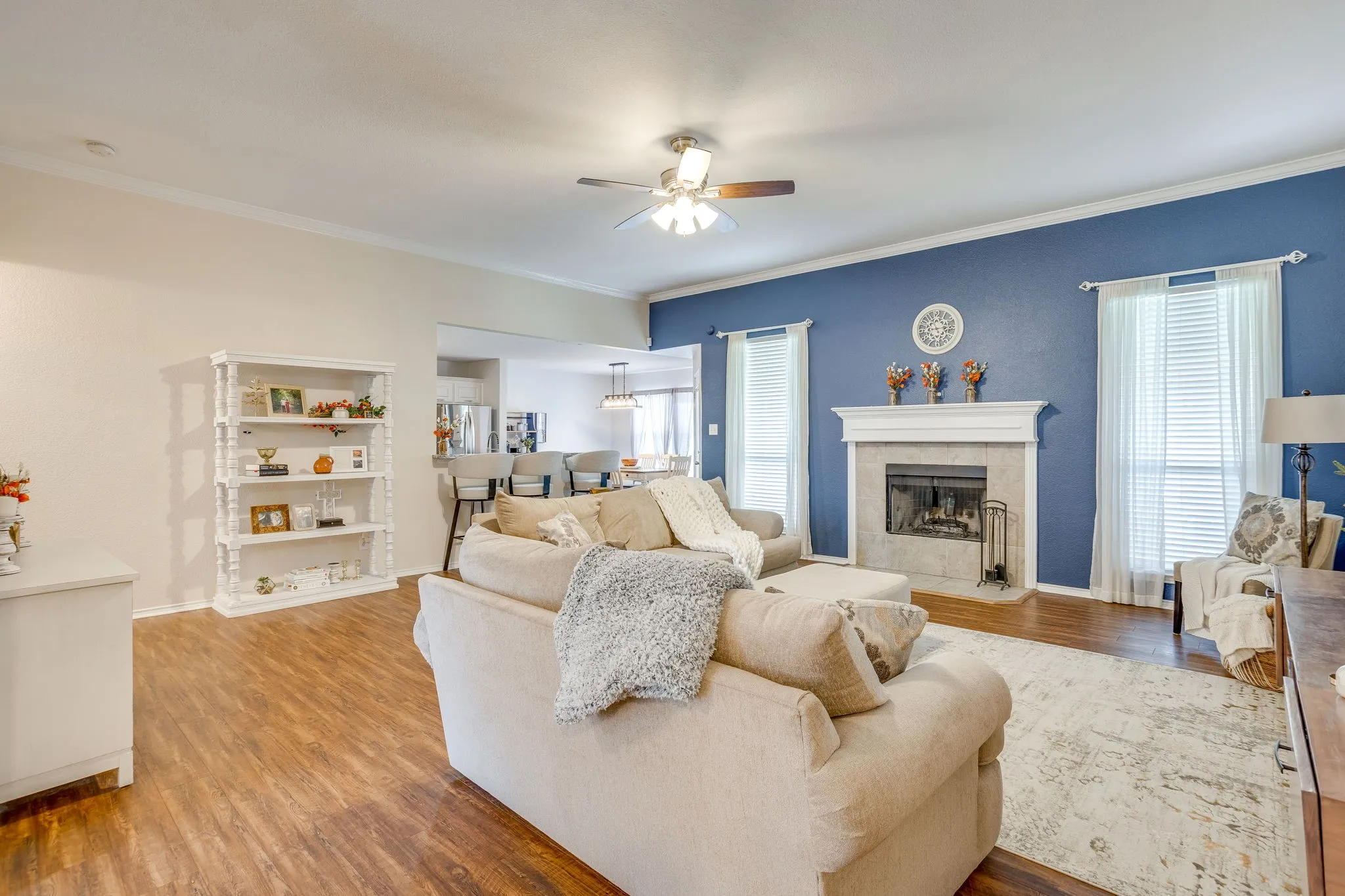 Living room featuring neutral light pain on the main wall and a deep blue accent wall behind the fireplace, with medium-toned wood-style flooring throughout.