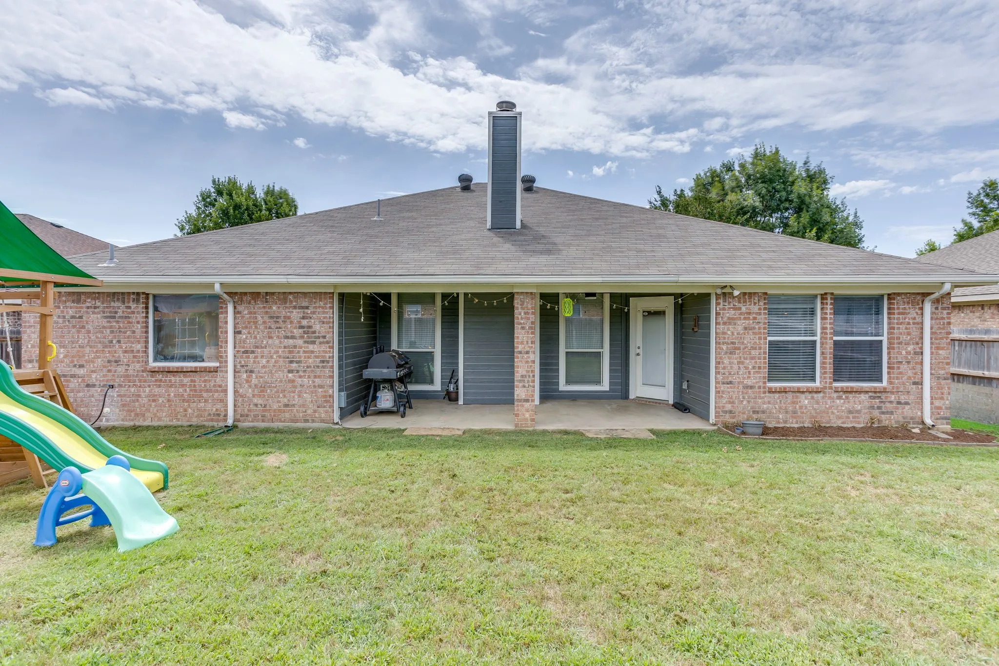 Back of house featuring a modern style hip roof and covered patio with brick column, and entry into the dining area and kitchen.