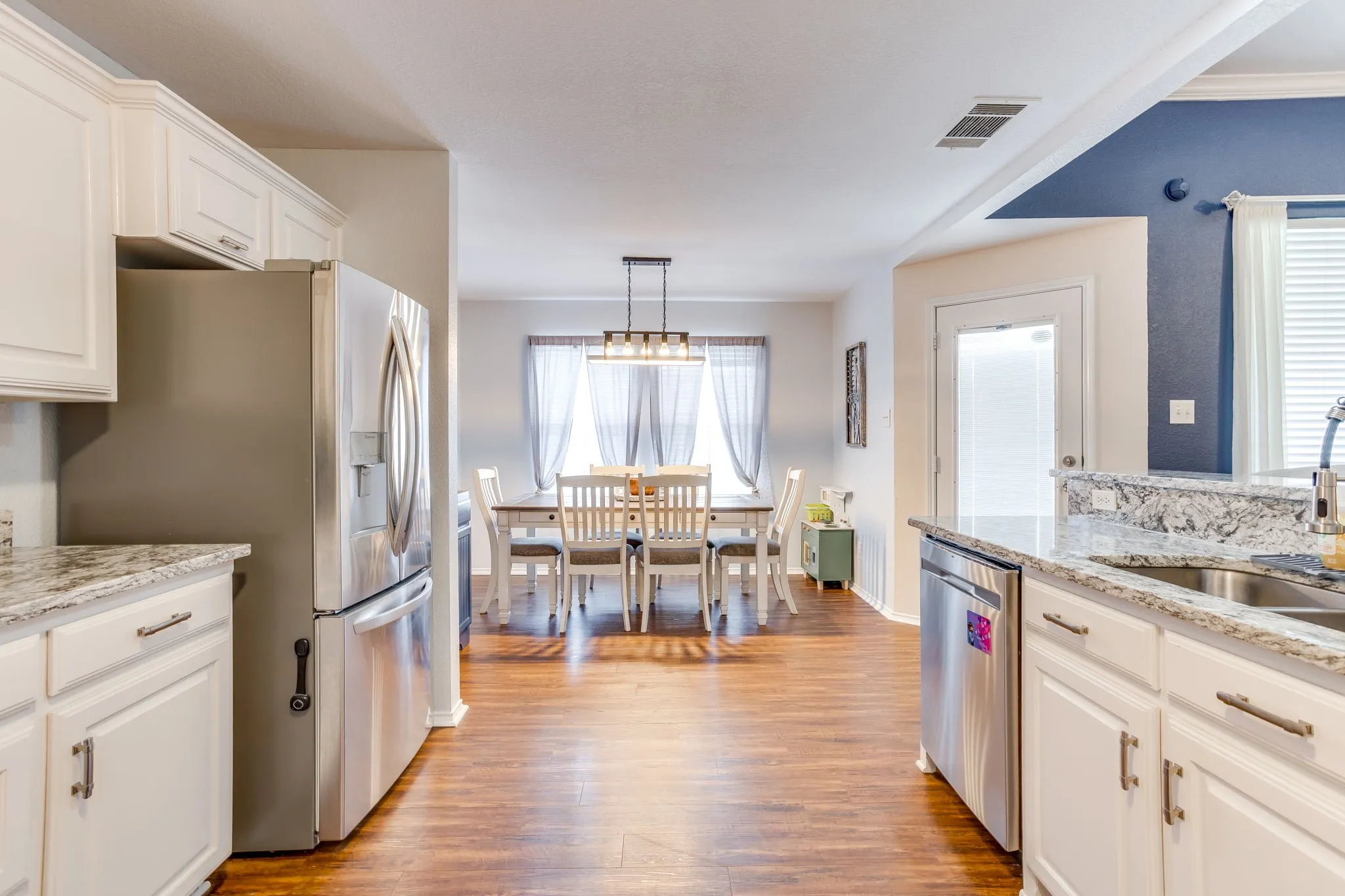 Kitchen featuring an under-mount stainless steel sink and luxury vinyl plank flooring that flows continuously into the dining area, and a french door refrigerator.